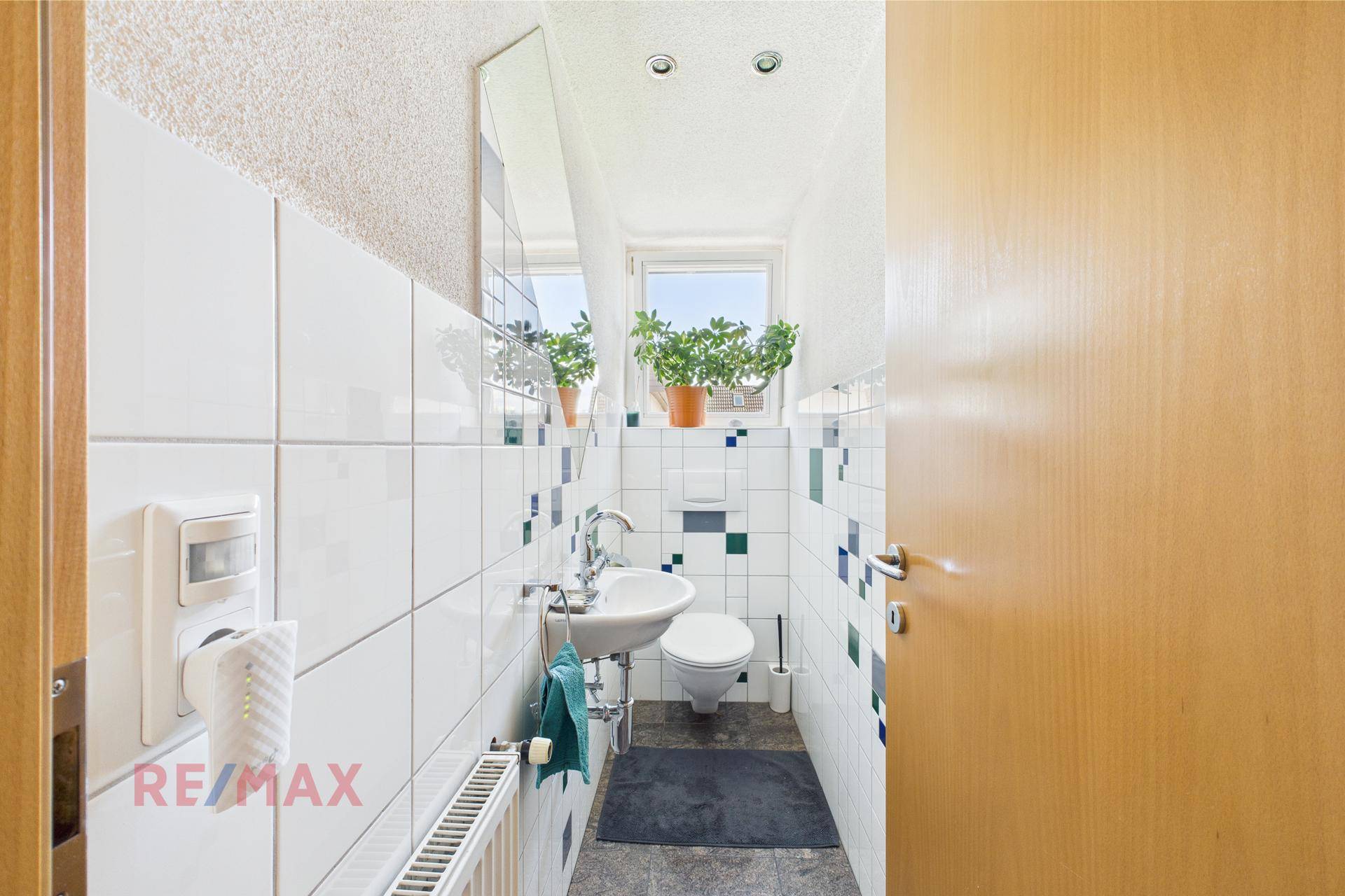 Kleines Gäste-WC mit Fenster, Waschbecken und weißen Fliesen mit blauen Akzenten.