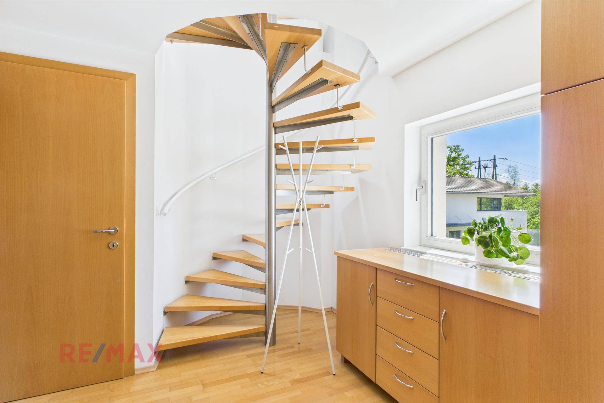 Heller Flur mit Holztreppe, Holzschränken und Fenster mit Blick ins Grüne.