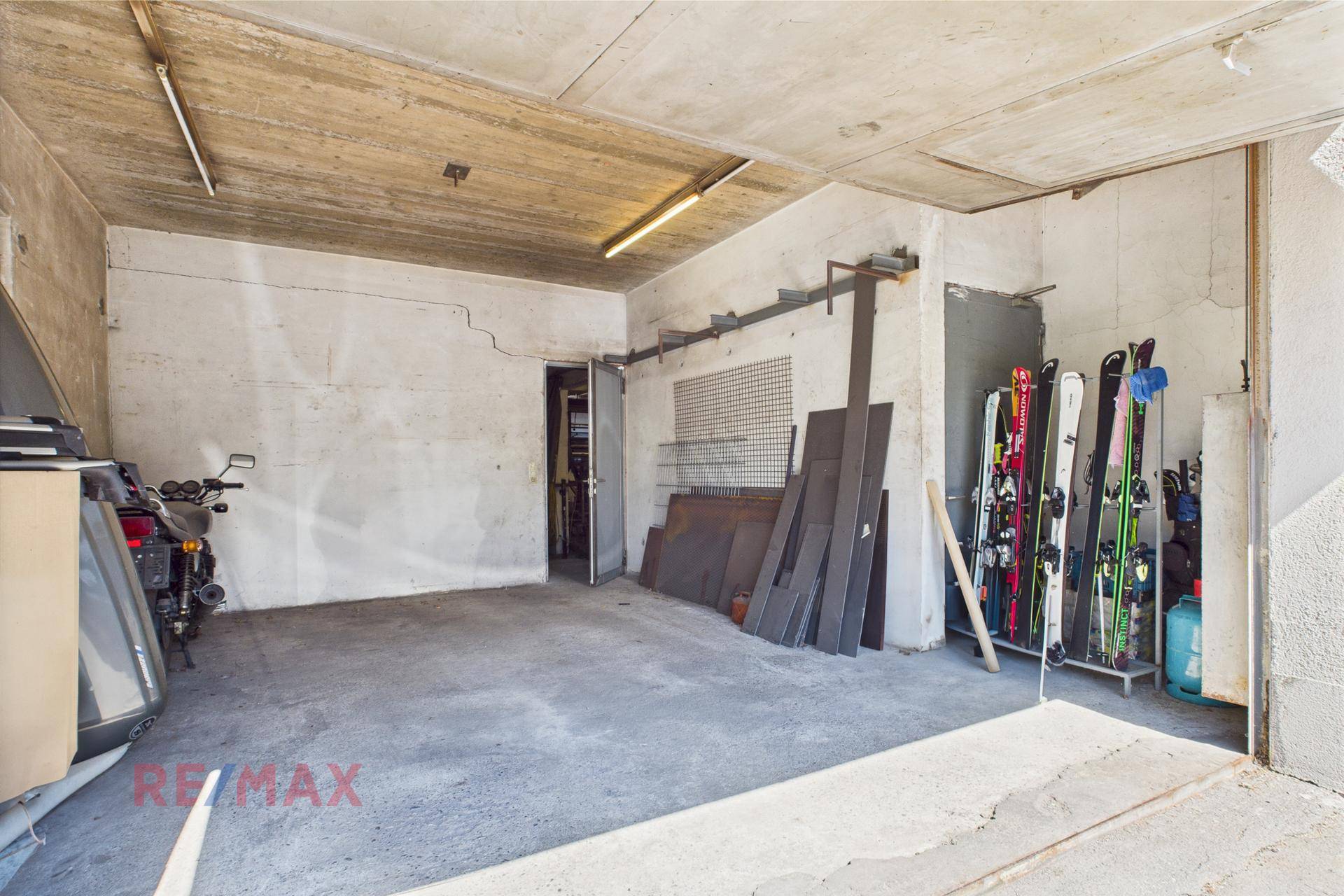 Geräumige Garage mit Betonboden, Skiern und Motorrad für Lagerung und Fahrzeuge.