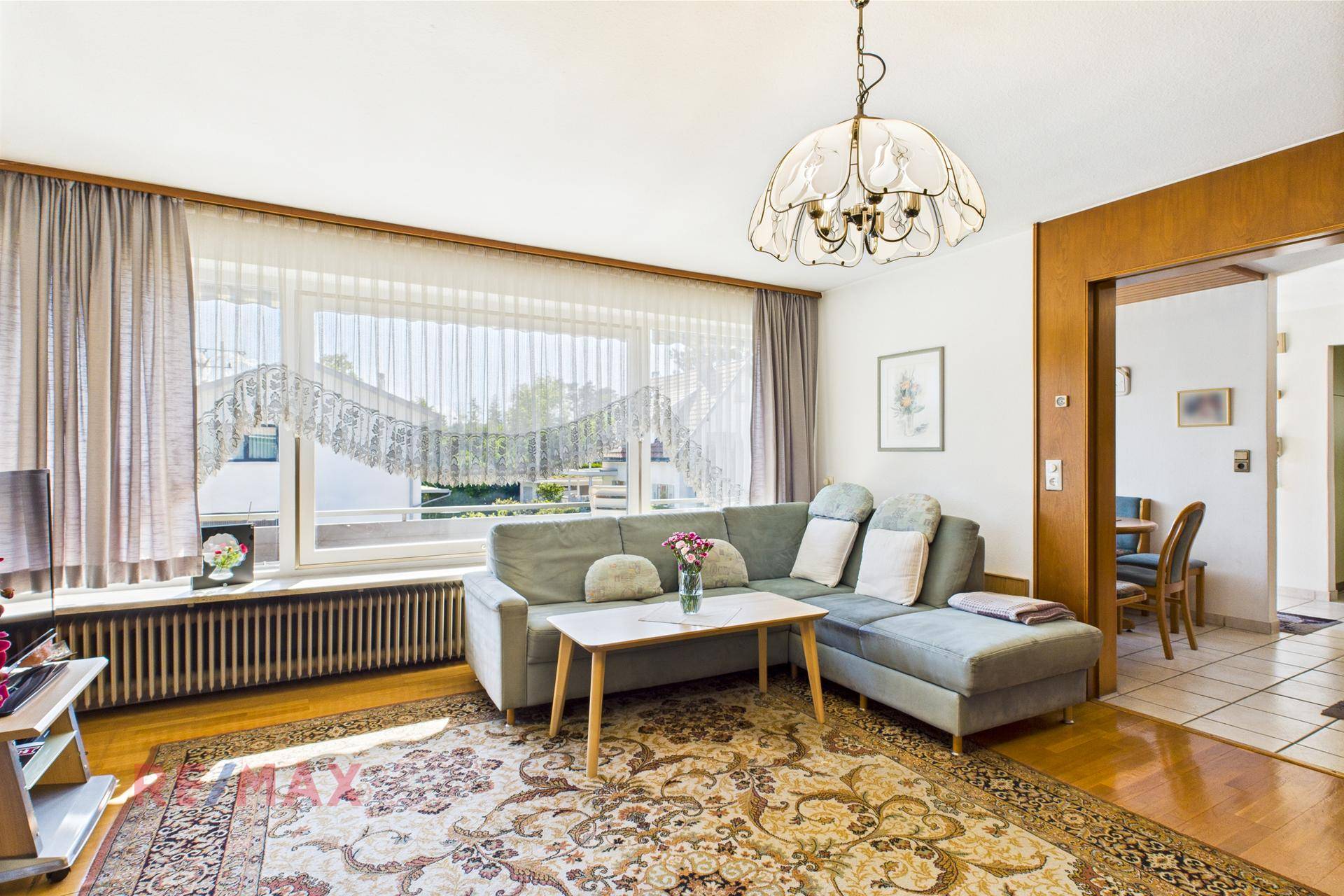 Gemütliches Wohnzimmer mit grauem Sofa, großem Fenster und Teppich auf Parkettboden.