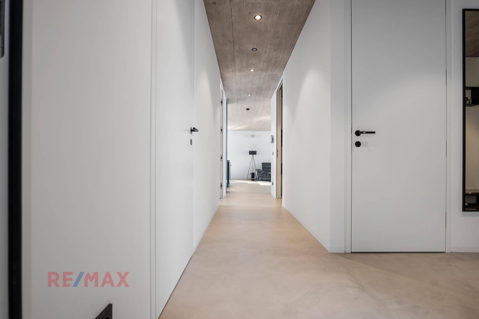Langer, heller Flur mit minimalistischem Design und Betonoptikdecke, der zu weiteren Räumen führt.