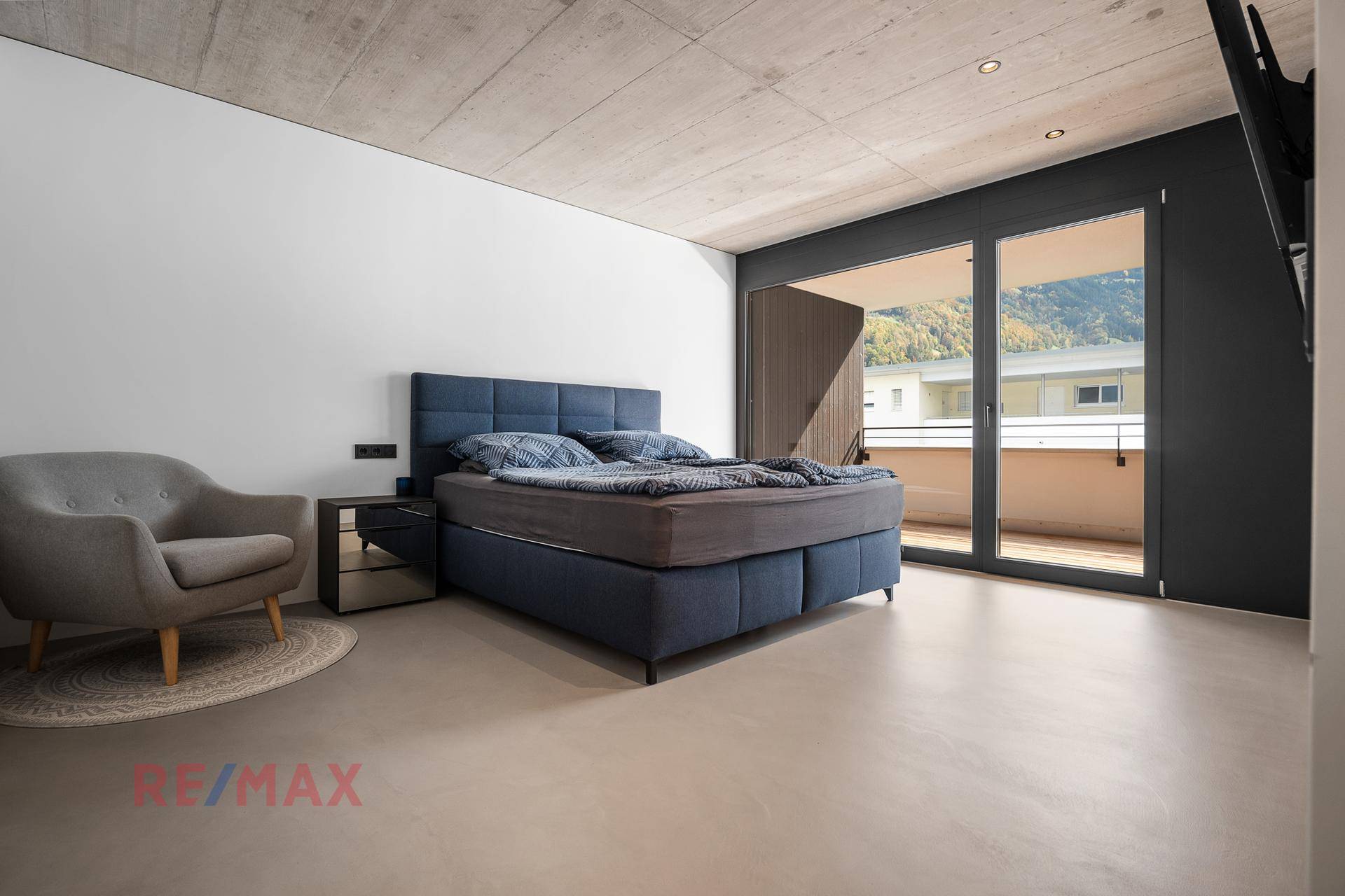 Modernes Schlafzimmer mit Doppelbett, Balkonzugang und Bergblick durch bodentiefe Fenster.