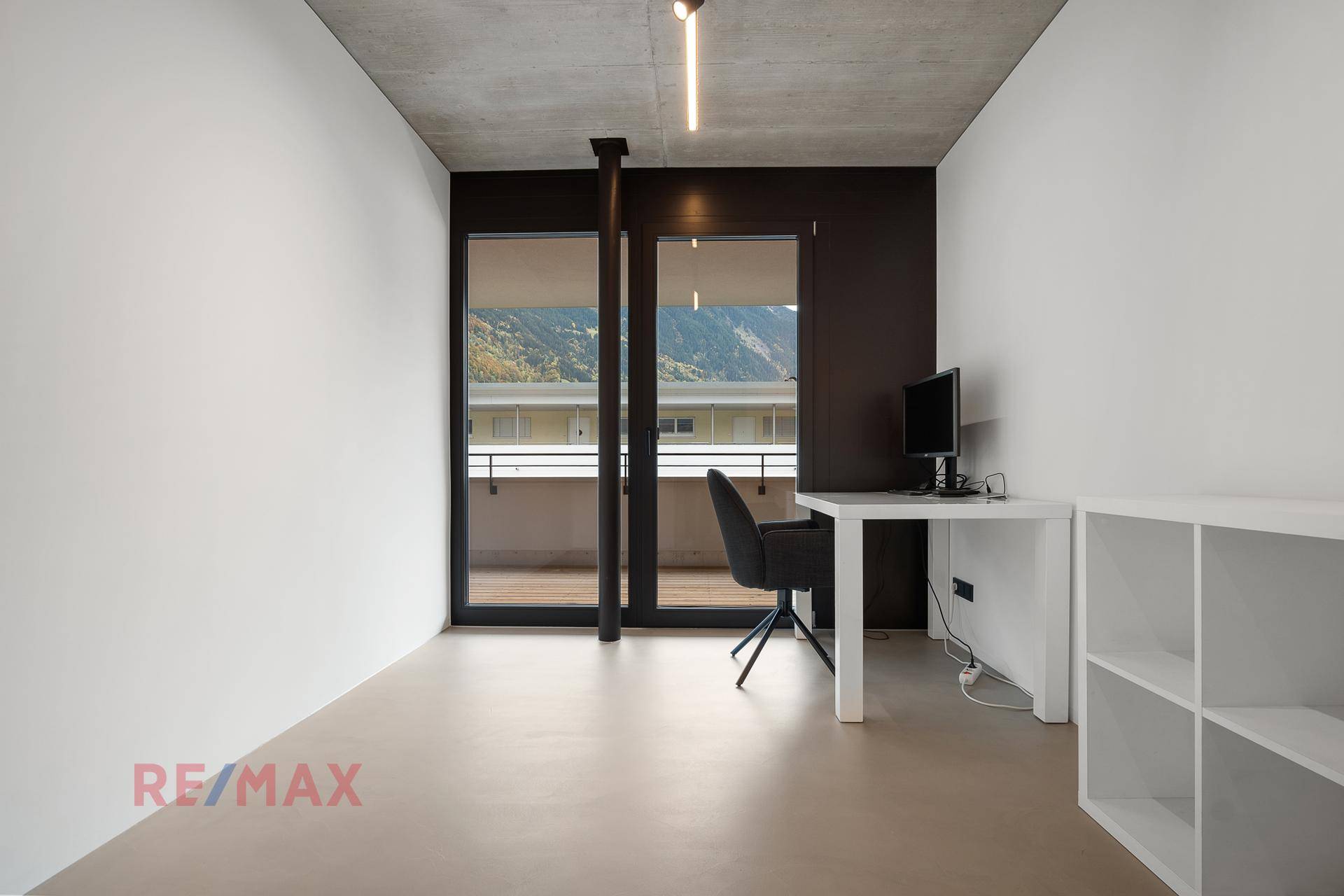 Helles Arbeitszimmer mit Schreibtisch und Zugang zum Balkon mit Bergblick.