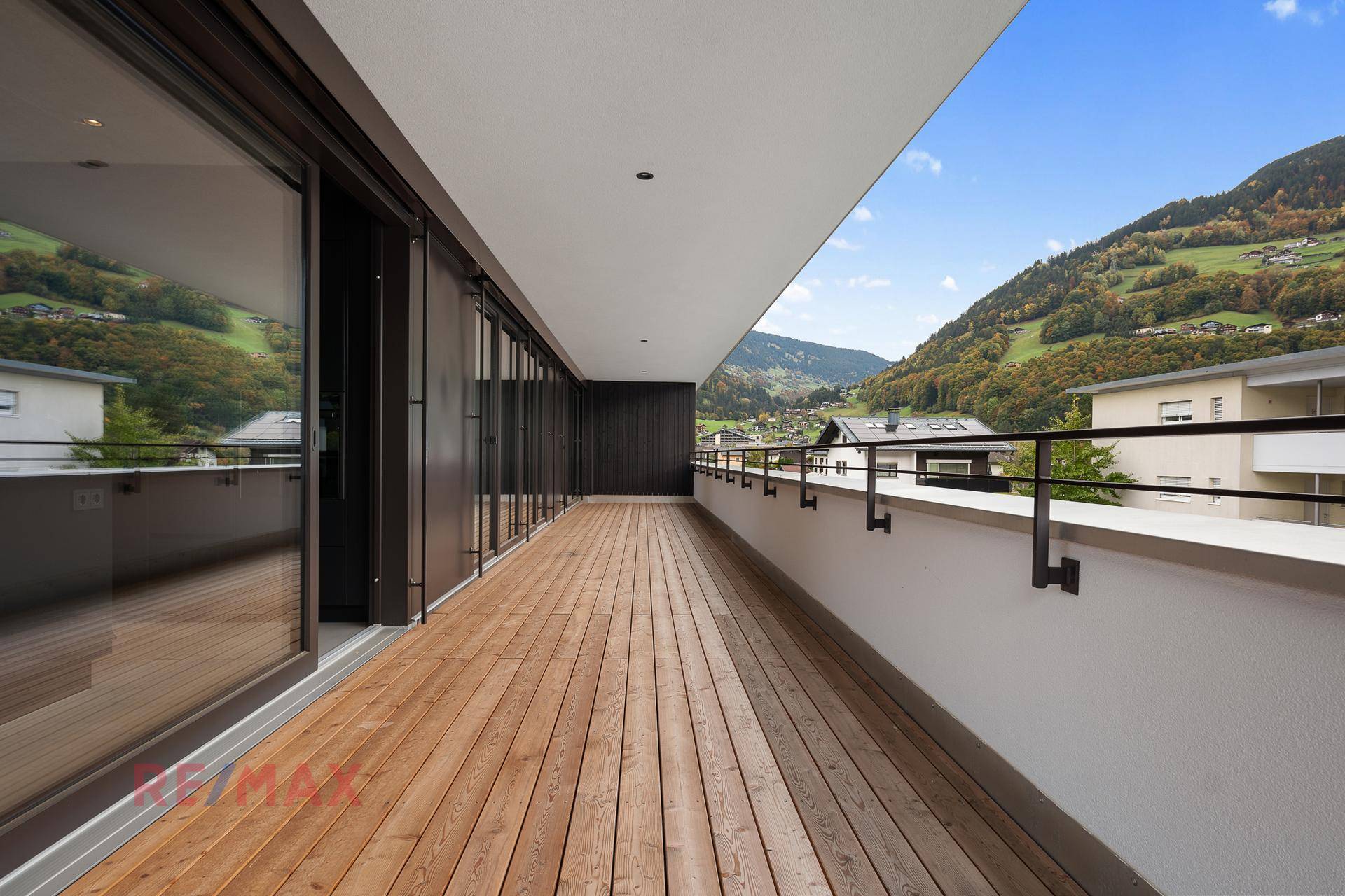 Geräumiger Holzbalkon mit weitem Blick auf die Berge und grüne Hügel unter blauem Himmel.