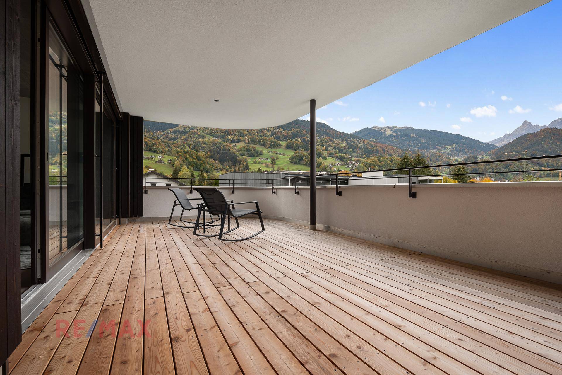 Großer Balkon mit Holzbelag, Sitzgelegenheiten und Panoramablick auf die Berge.