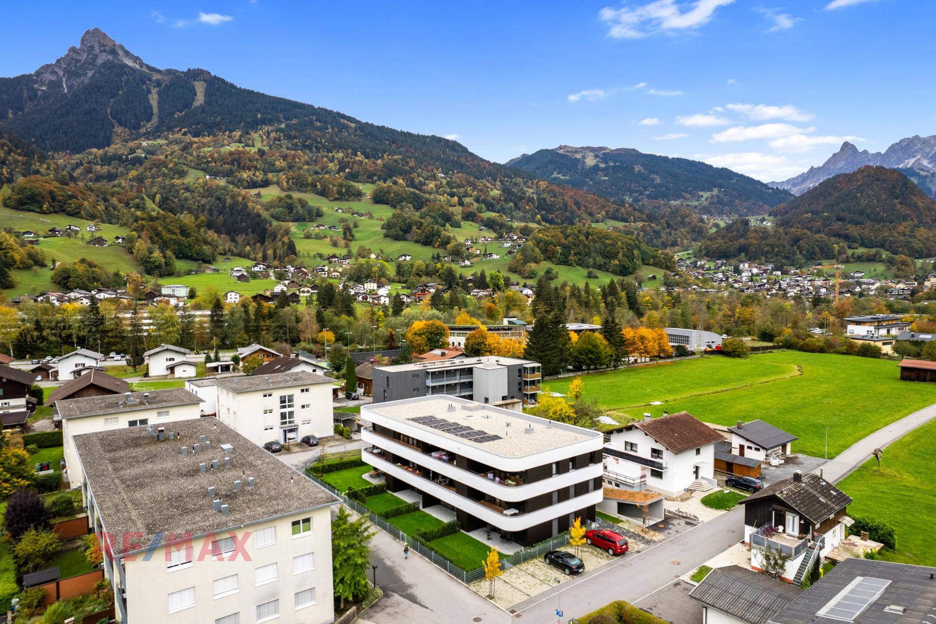 Luftaufnahme eines modernen Wohngebäudes in einer grünen Berglandschaft mit Photovoltaikanlage.