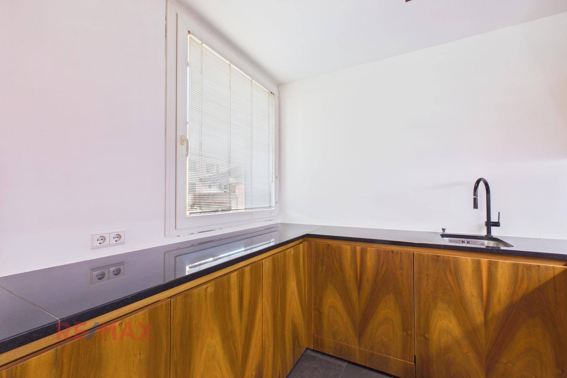 Helle Küche mit Holzschränken, dunkler Arbeitsplatte und Fenster für Tageslicht.