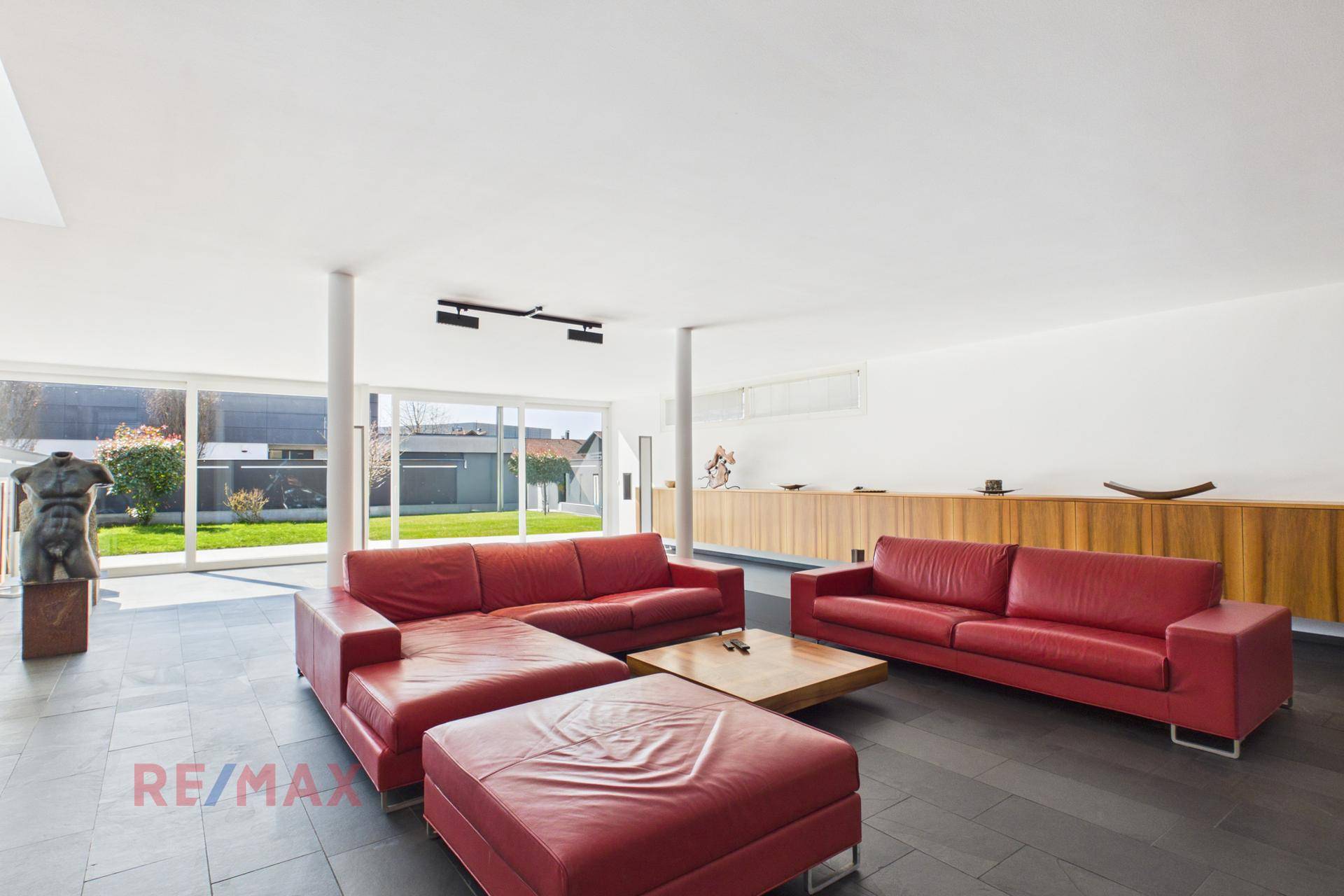 Großzügiges Wohnzimmer mit roten Ledersofas, dunklem Fliesenboden und viel Tageslicht.