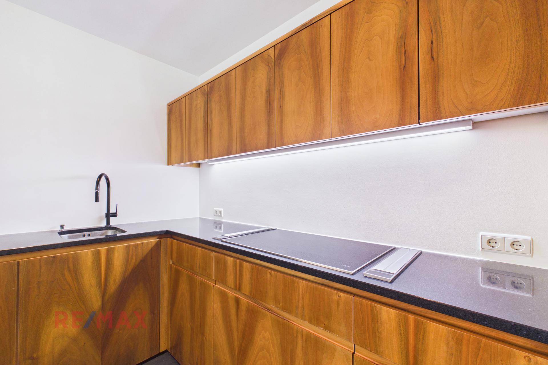 Moderne Küche mit Holzfronten, dunkler Arbeitsplatte und Induktionskochfeld.