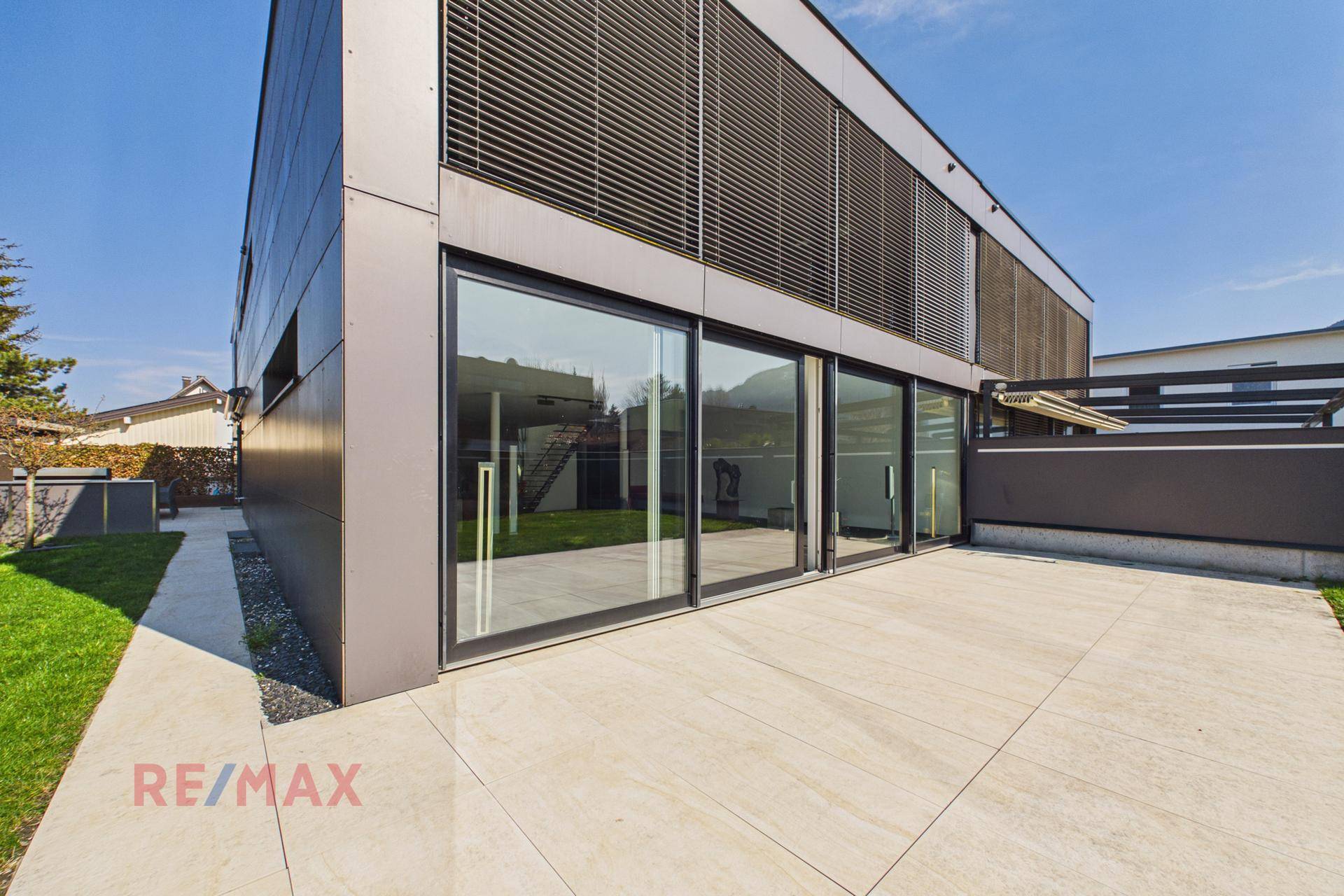Moderne Gebäudefassade mit großen Glasfronten und einer hellen, gefliesten Terrasse.