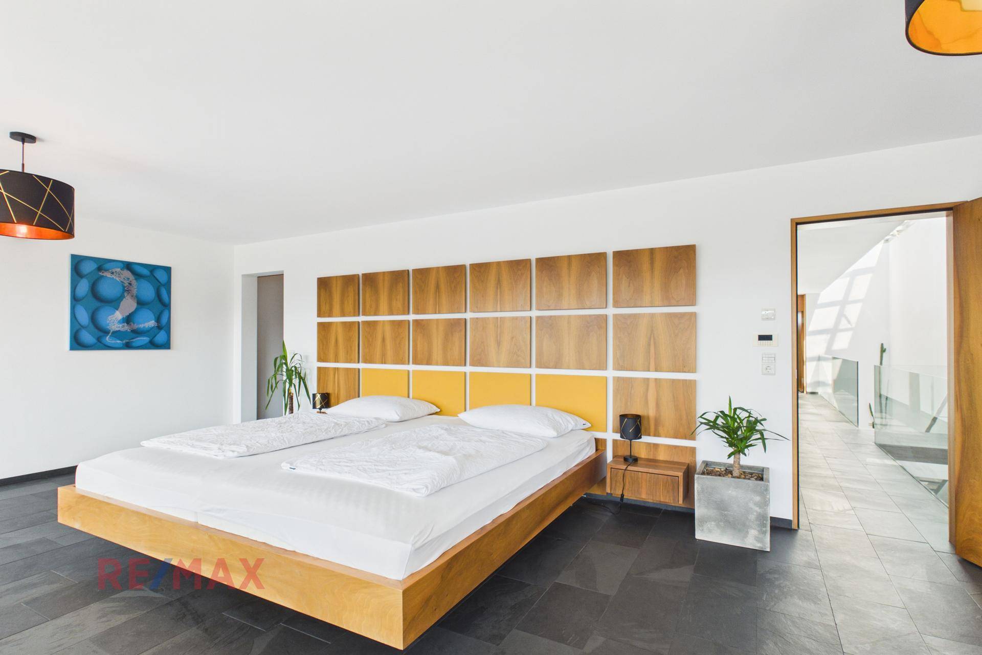 Modernes Schlafzimmer mit großem Bett, Holzelementen und dunklem Fliesenboden.
