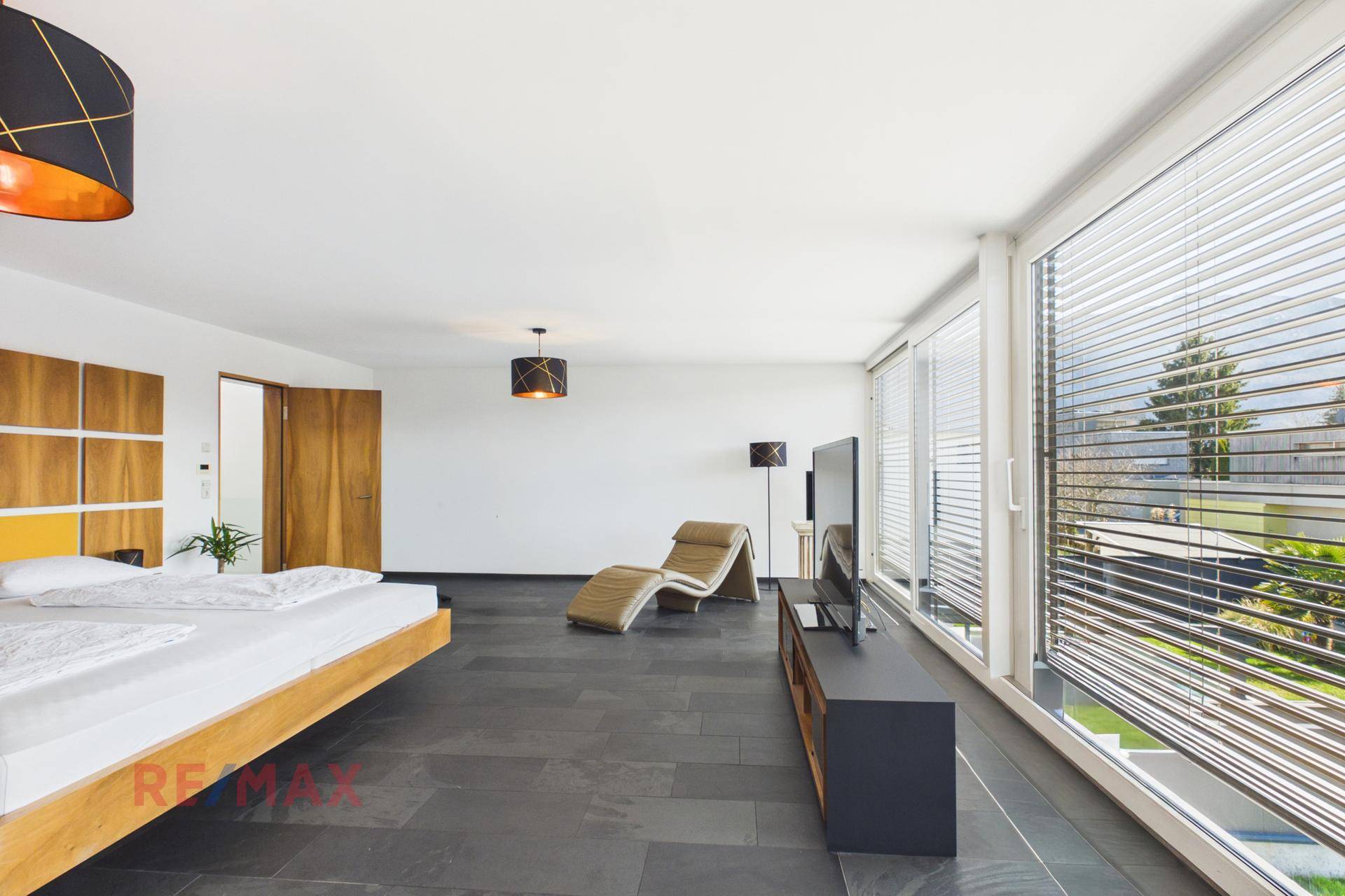 Helles Schlafzimmer mit bodentiefen Fenstern, Liege und Blick ins Grüne.