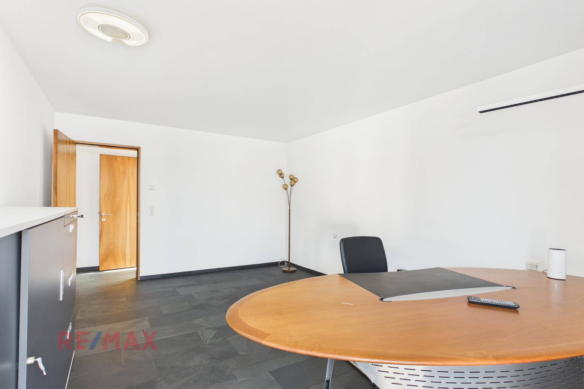 Helles Büro mit großem Schreibtisch und dunklem Fliesenboden.