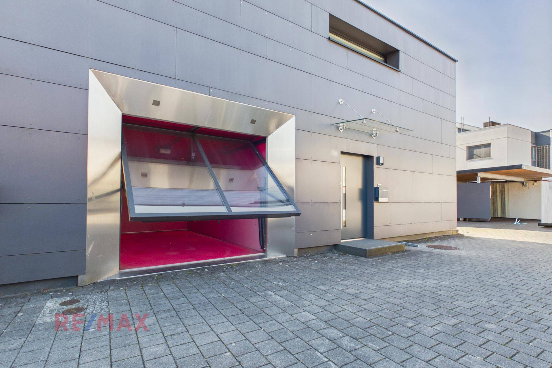 Moderne Gebäudefassade mit integriertem Autolift und Eingangsbereich.