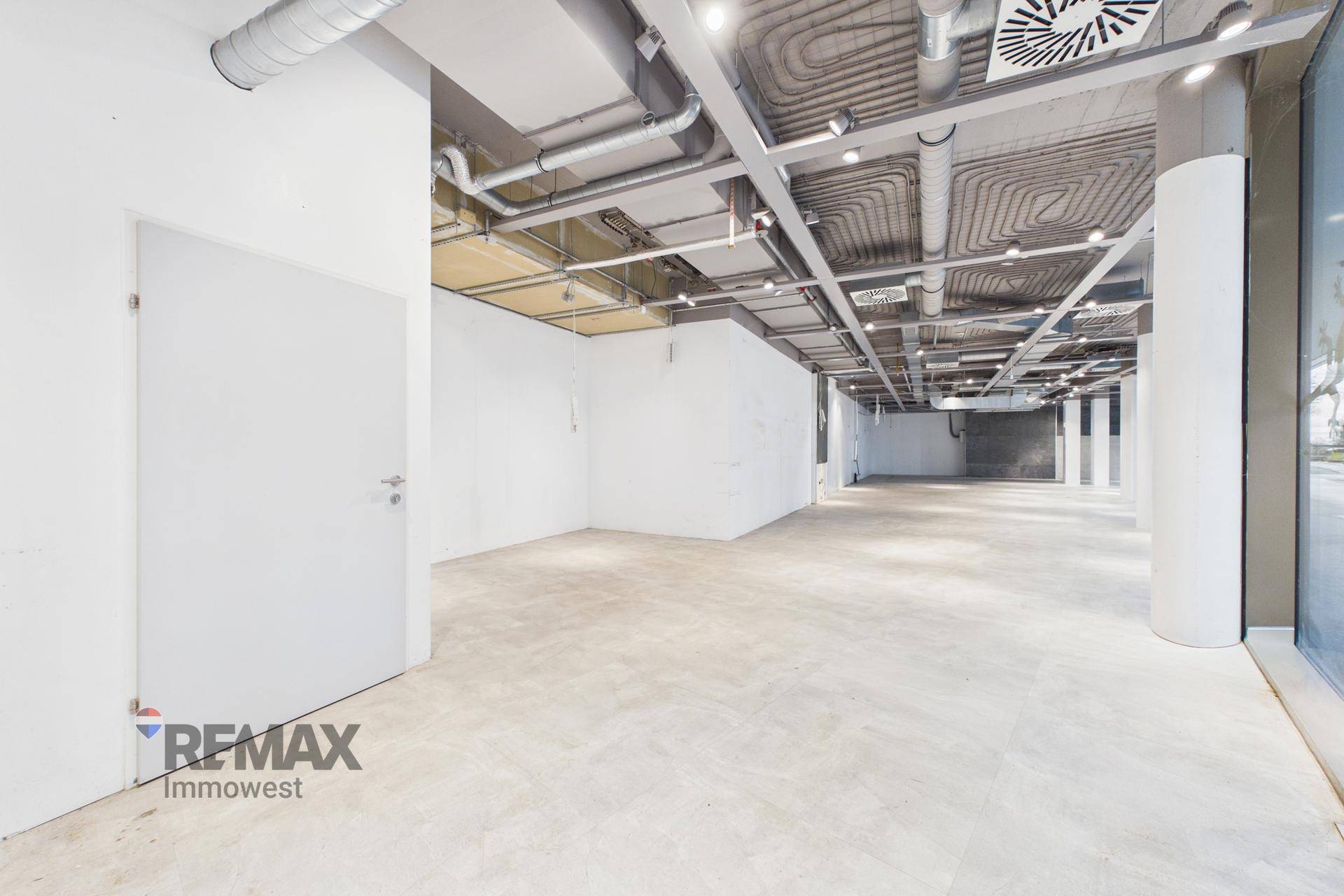 Heller, leerer Geschäftsraum mit Betonboden, weißen Wänden und sichtbaren Deckeninstallationen, bereit für den Ausbau.