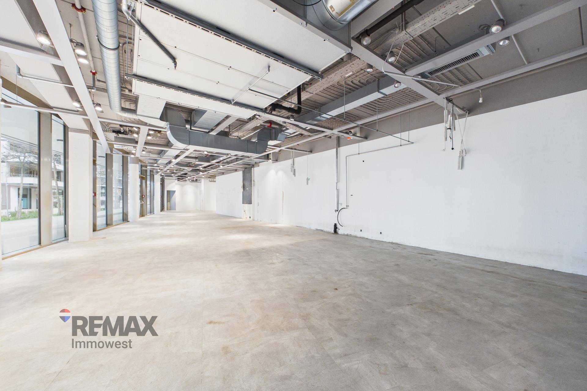 Langer, leerer Geschäftsraum mit Betonboden, weißen Wänden und sichtbaren Deckeninstallationen, ideal für flexible Nutzung.