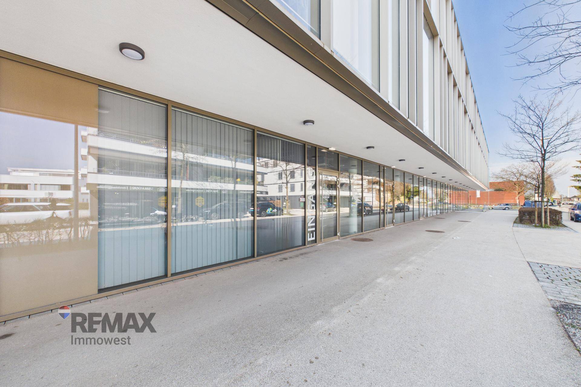 Nahaufnahme der modernen Geschäftsfassade im Erdgeschoss mit großen Schaufenstern und breitem Gehweg.