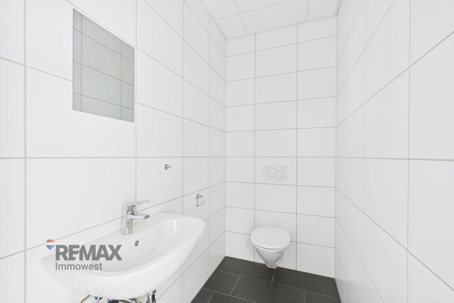 Modernes WC mit weiß gefliesten Wänden, dunklem Boden und wandhängender Toilette und Waschbecken.