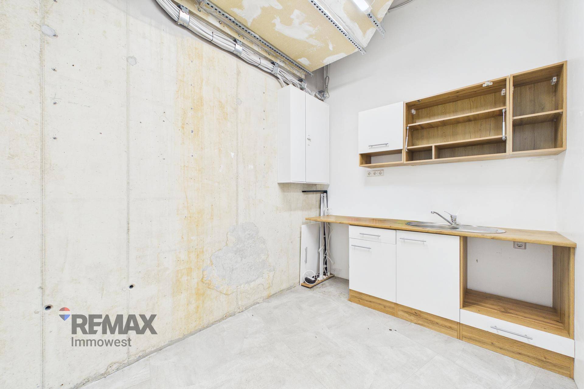 Einfache Küchenzeile mit Holz-Arbeitsplatte, weißen Schränken und offenen Regalen in einem kleinen Raum.