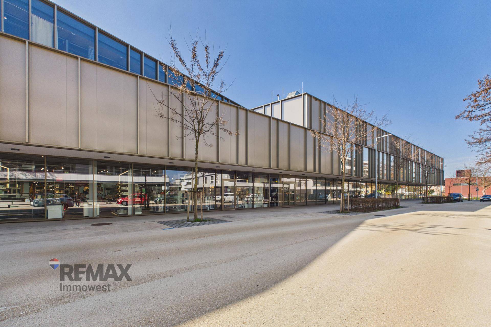 Weitläufige Ansicht der modernen Geschäftsfassade mit großen Glasflächen unter blauem Himmel und umliegender Infrastruktur.