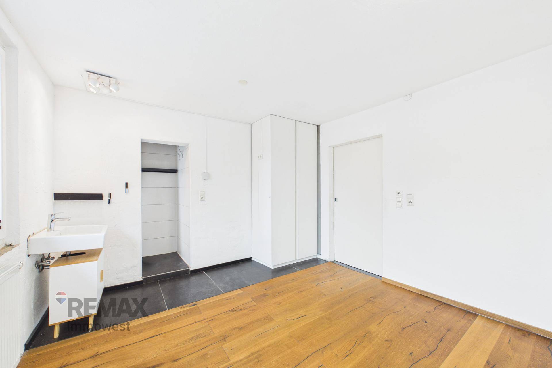Helles Zimmer mit Holzboden, Waschbecken und einem Duschbereich, ideal für ein kleines Bad.