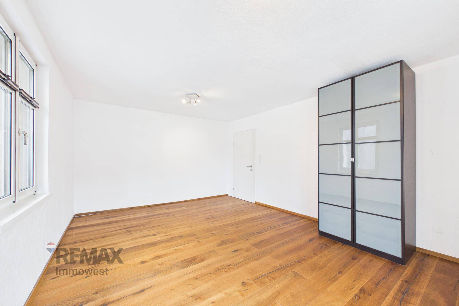 Geräumiges Zimmer mit Holzboden, weiß gestrichenen Wänden und einem modernen Schrank.