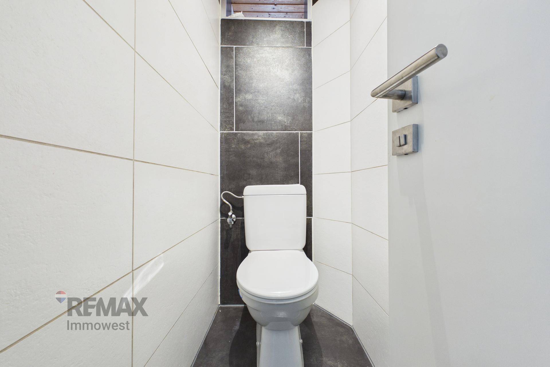Modernes Gäste-WC mit weißen und dunkelgrauen Fliesen sowie einer Wandtoilette.