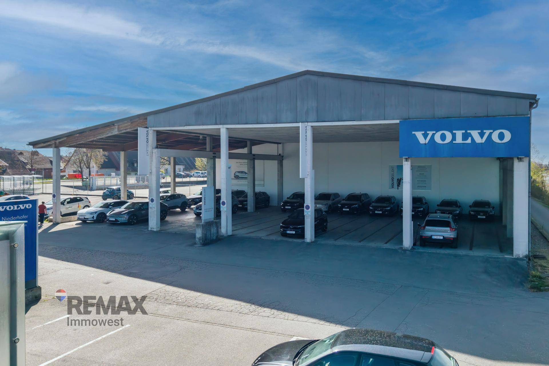 Überdachter Außenbereich eines Autohauses mit mehreren Fahrzeugen und dem Volvo-Logo unter einem klaren Himmel.