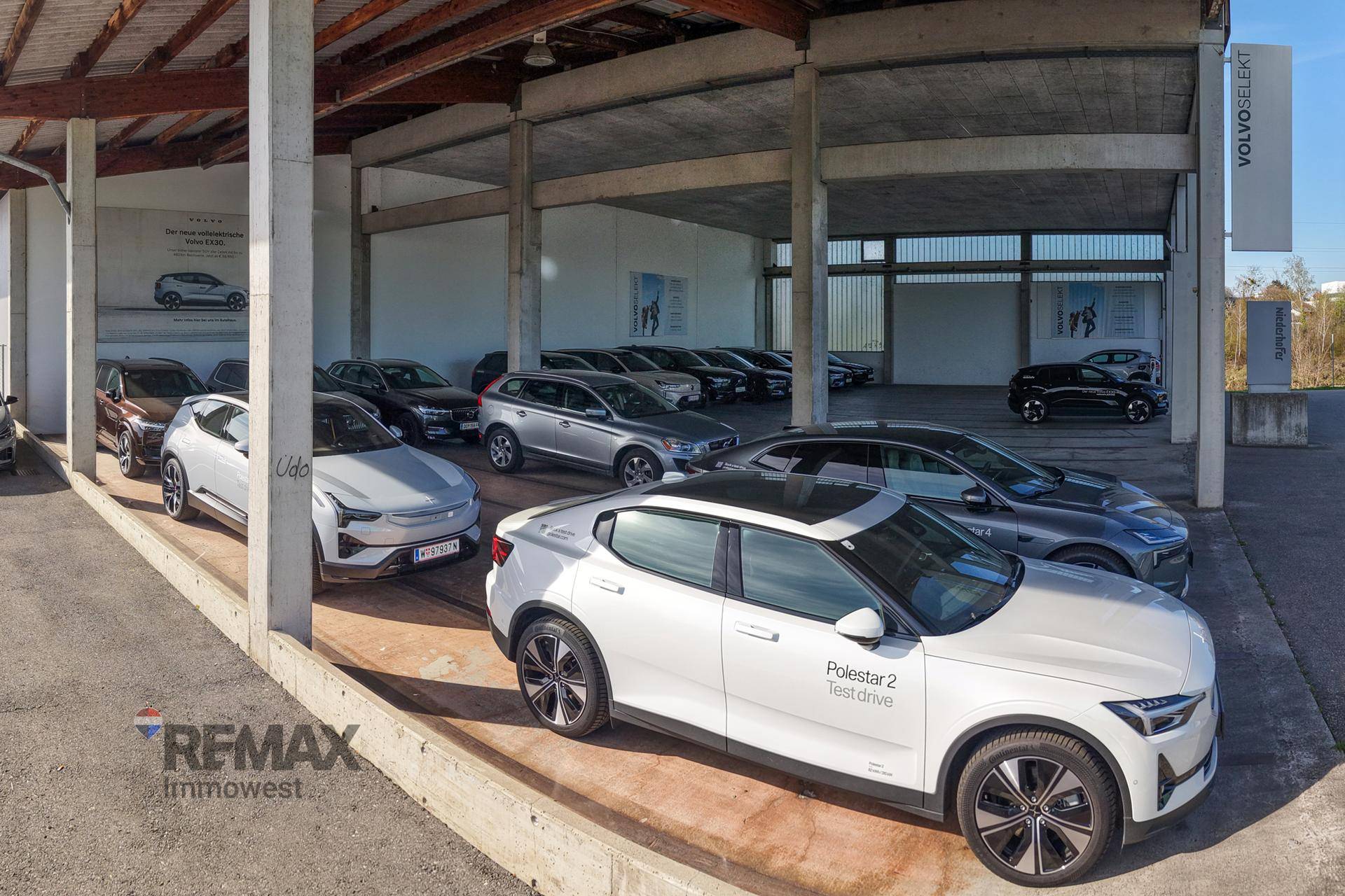 Nahaufnahme des überdachten Ausstellungsbereichs eines Autohauses mit modernen Fahrzeugen und Betonstützen.