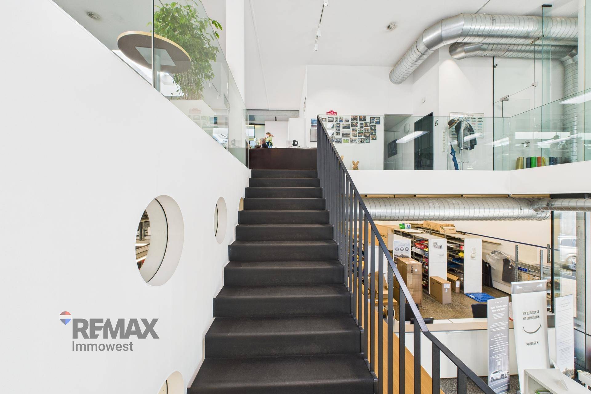 Moderne Treppe mit schwarzem Teppich und Metallgeländer, die zu einem oberen Bürobereich führt.