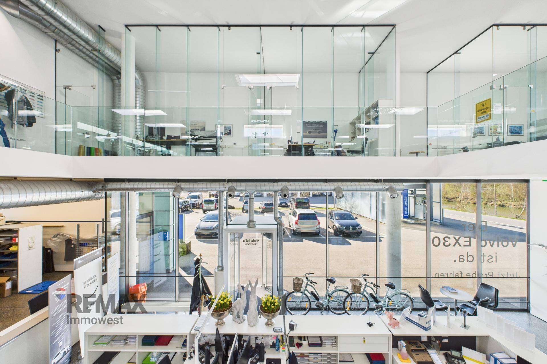 Offener Showroom-Bereich mit Blick auf die untere Etage und Glaswänden, die Büros abtrennen.