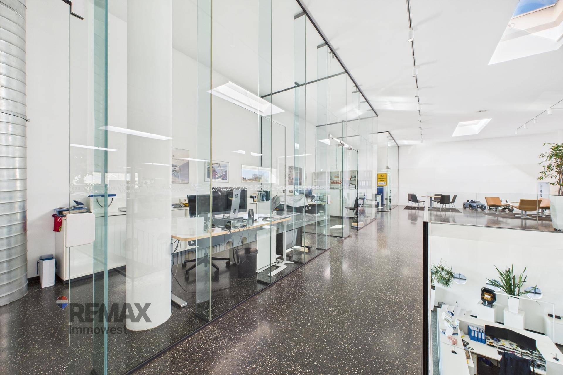 Moderner Bürobereich mit Glaswänden, Schreibtischen und Computern, der eine offene Arbeitsumgebung schafft.