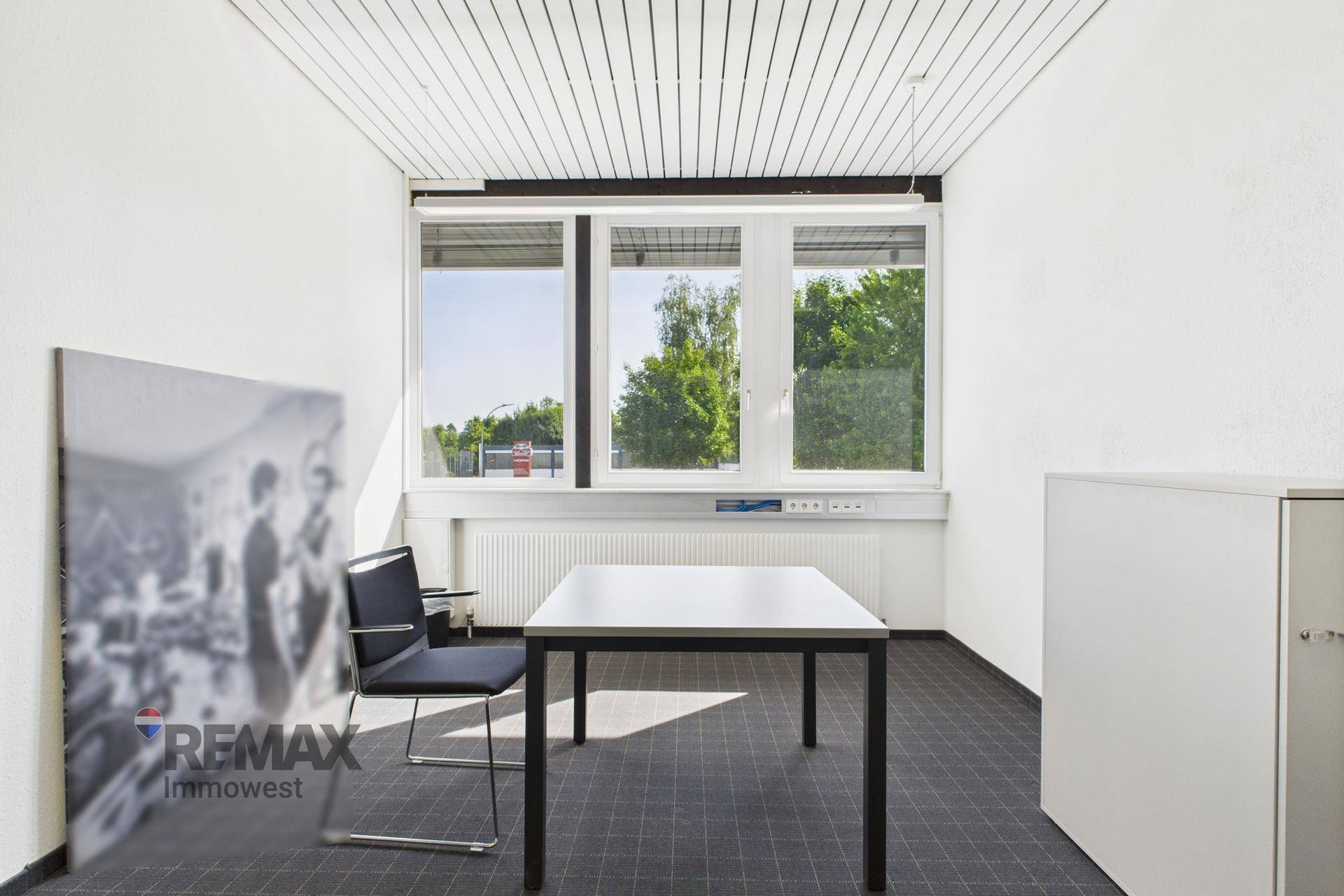 Kleines, helles Büro mit einem einzelnen Schreibtisch, Stuhl und großen Fenstern, die viel Tageslicht hereinlassen.