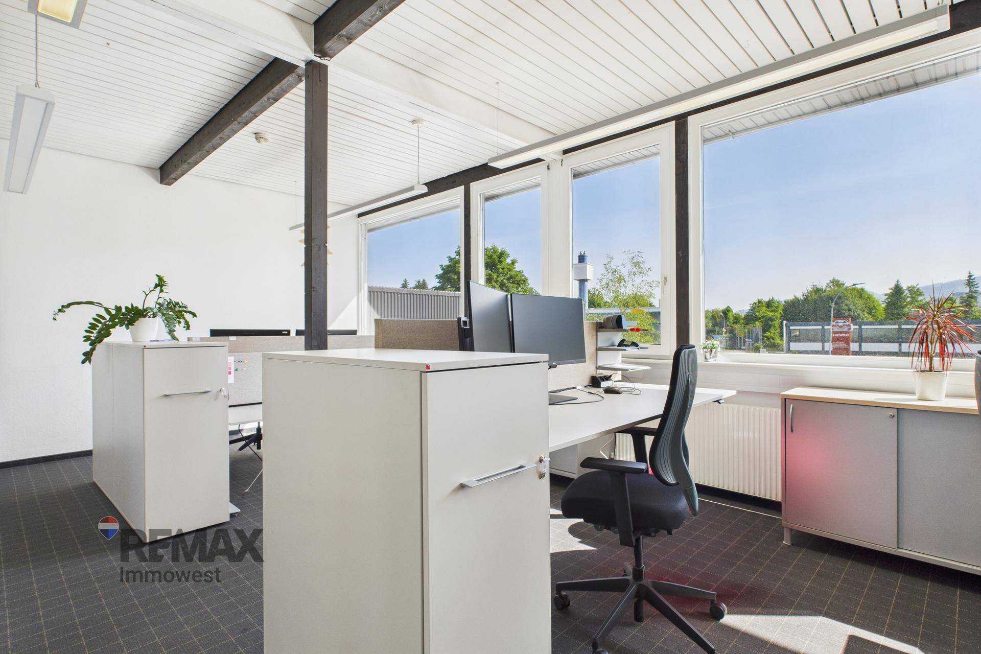 Heller Arbeitsplatz in einem modernen Büro mit großen Fenstern und Blick ins Grüne.