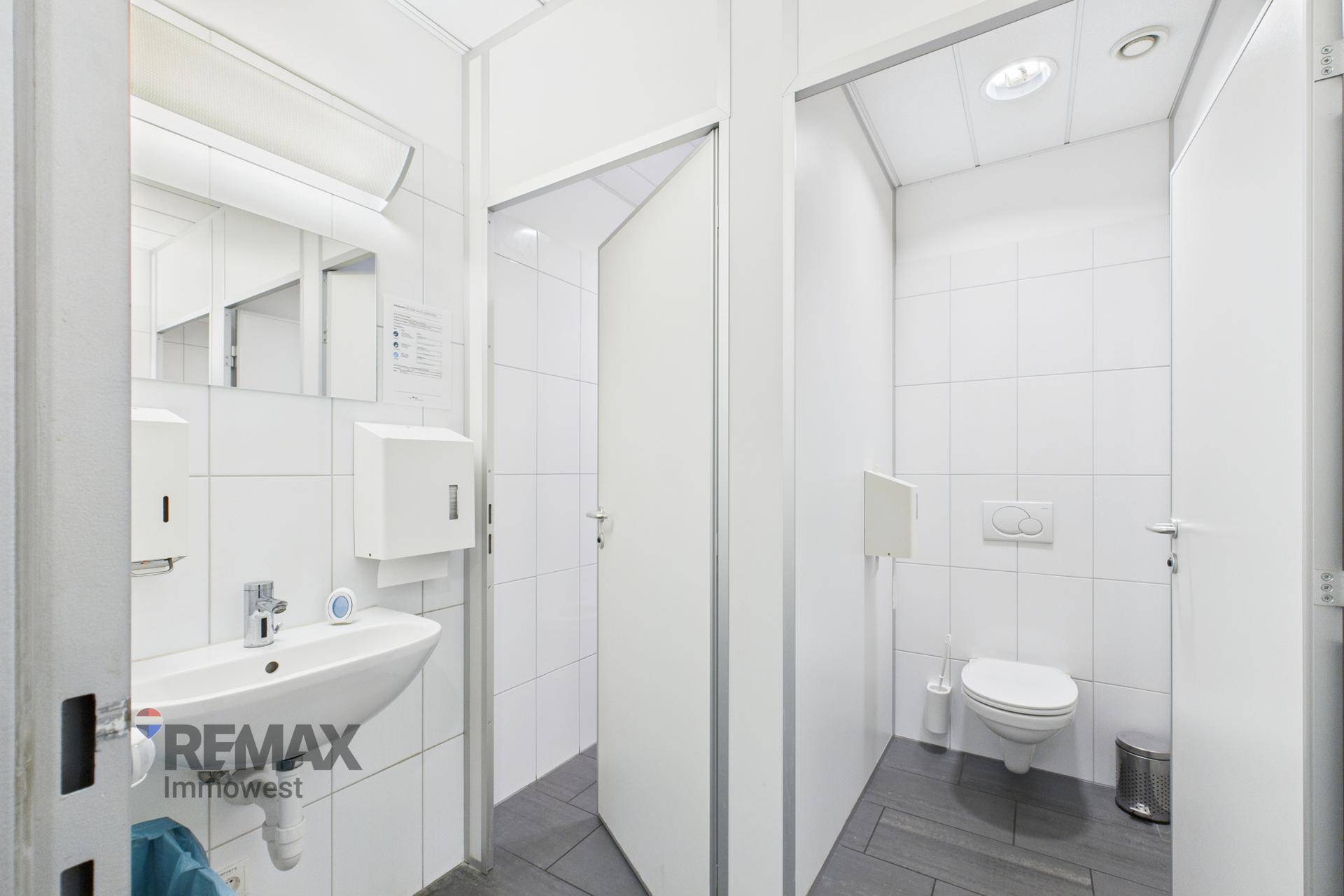 Saubere Toilettenanlage mit weißen Fliesen, Waschbecken und separaten Kabinen.