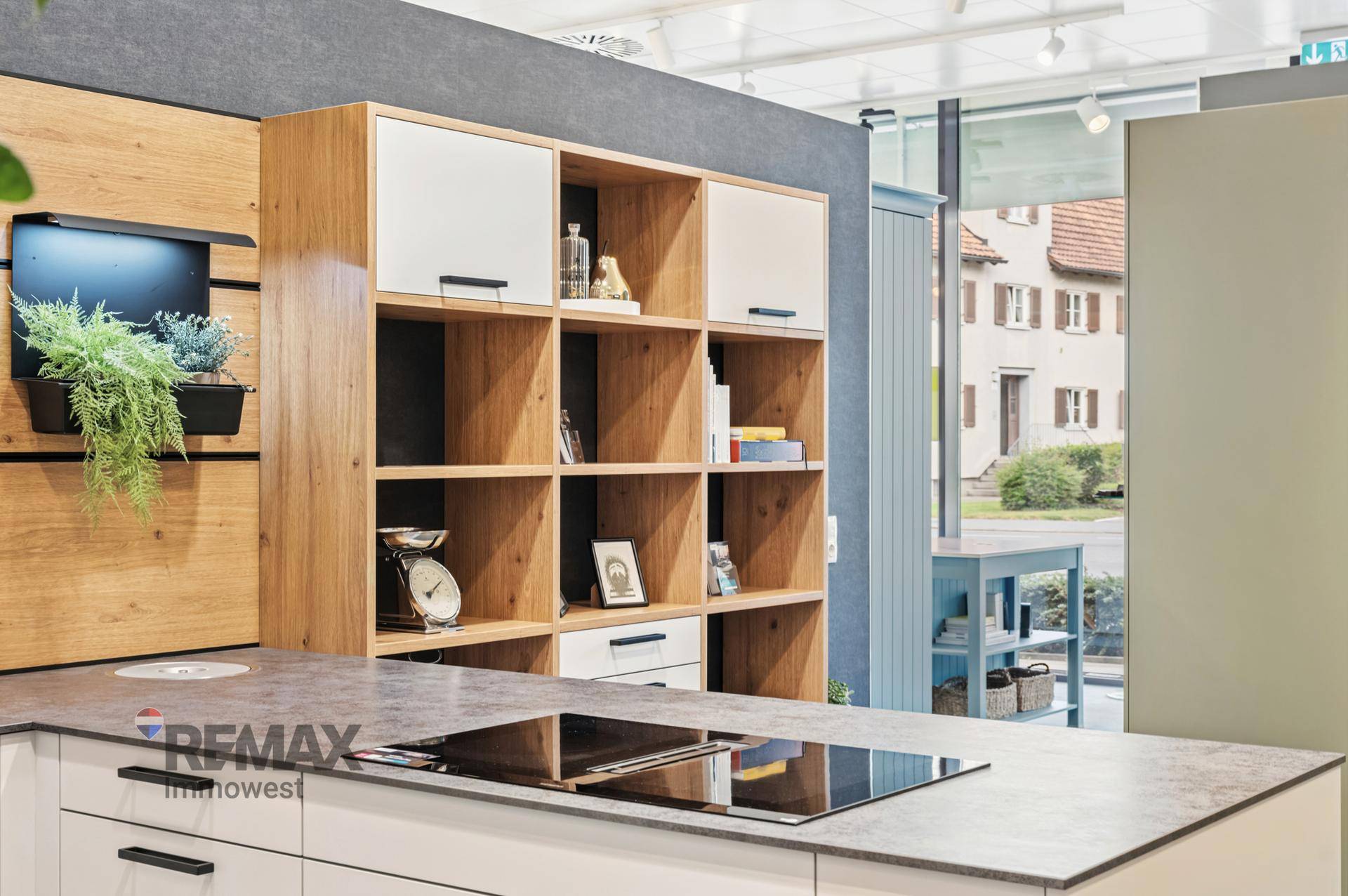 Detailansicht einer modernen Kücheninsel mit Kochfeld und offenem Holzregal in einem Ausstellungsraum.