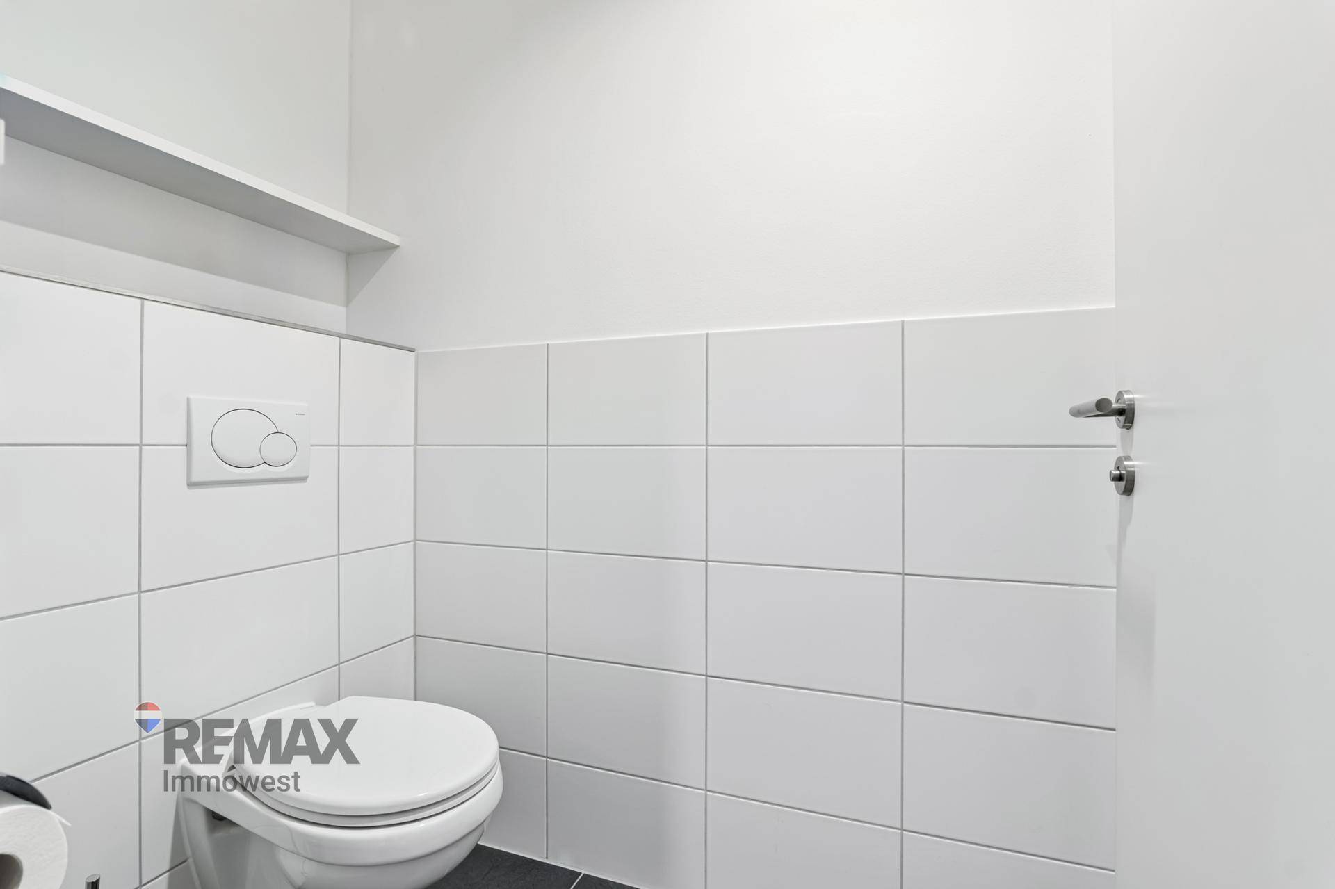 Saubere und moderne Toilette mit weißen Fliesen und wandmontiertem WC in minimalistischem Design.