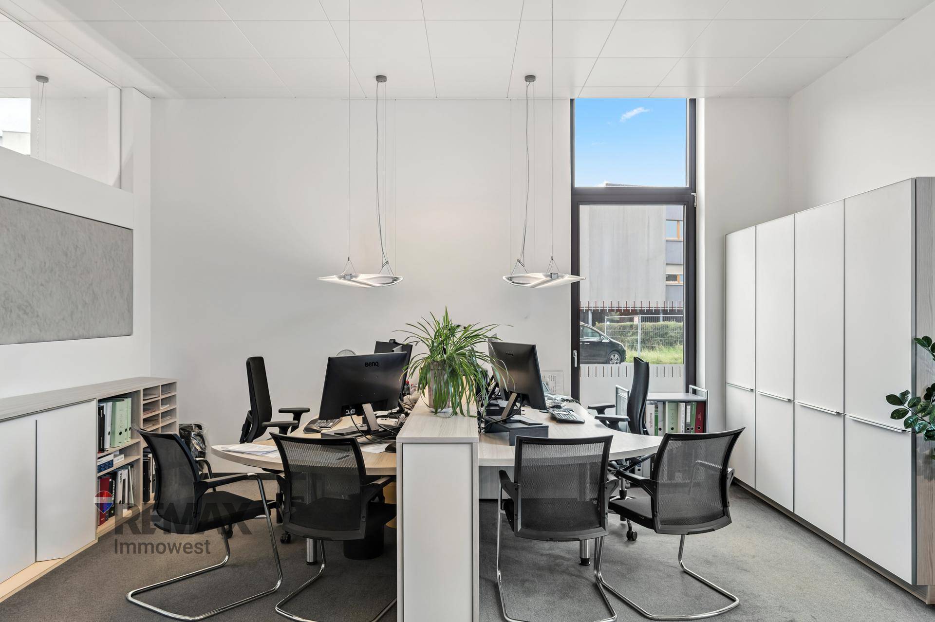 Modernes Büro mit mehreren Arbeitsplätzen, weißen Schränken und großen Fenstern für Tageslicht.