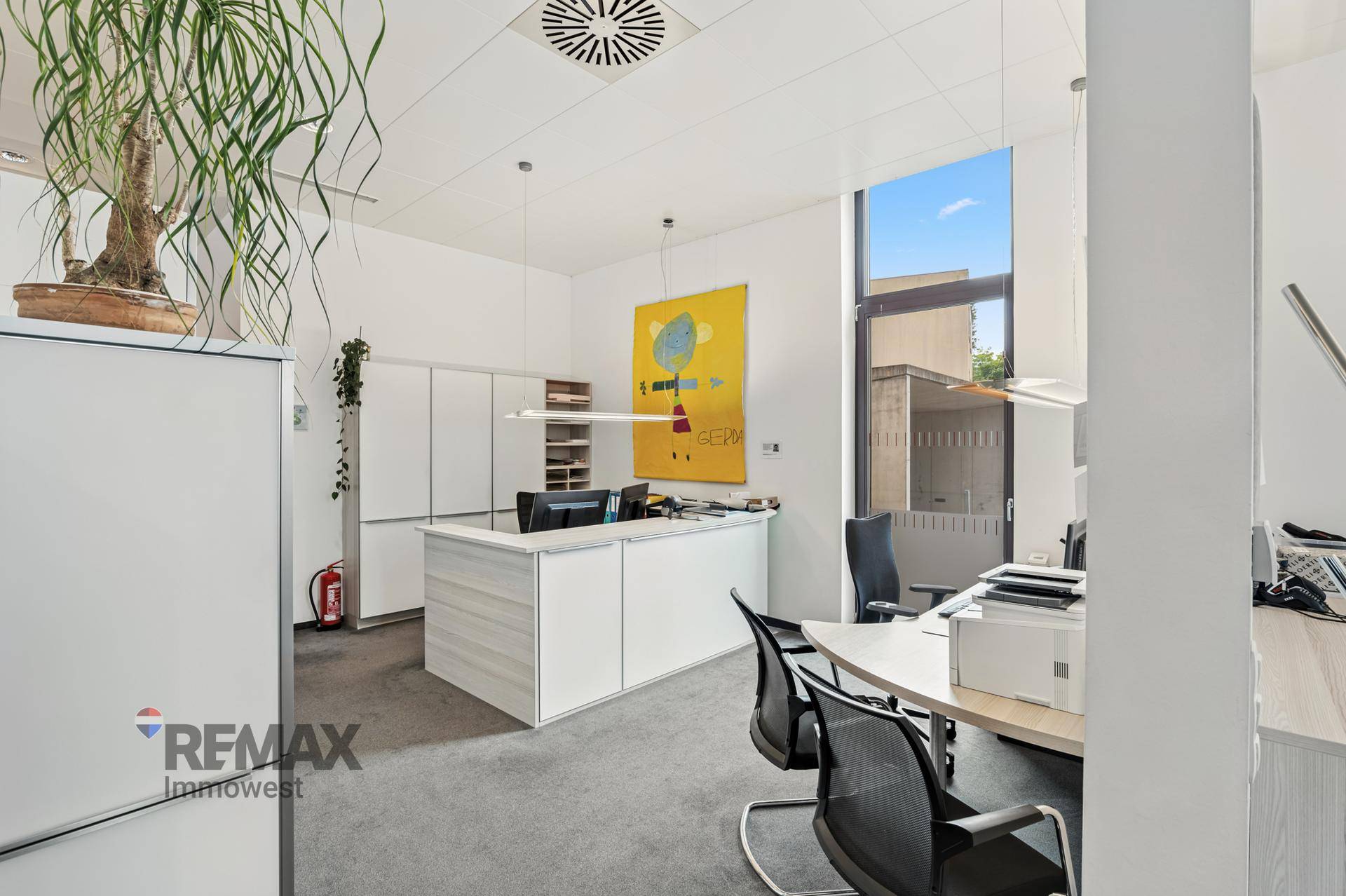 Helles und geräumiges Büro mit modernen Möbeln, weißen Schränken und einem farbigen Kunstwerk.