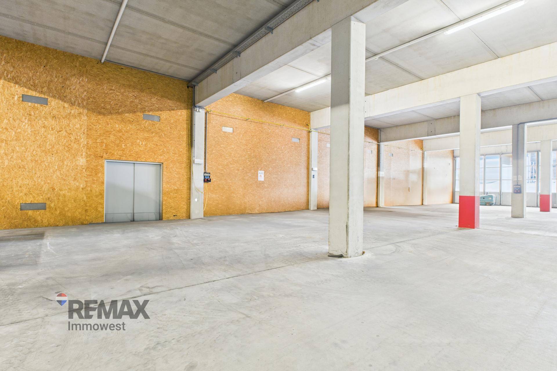 Geräumige Lagerhalle mit OSB-Plattenwänden und einer großen grauen Tür, die möglicherweise zu einem Aufzug führt.