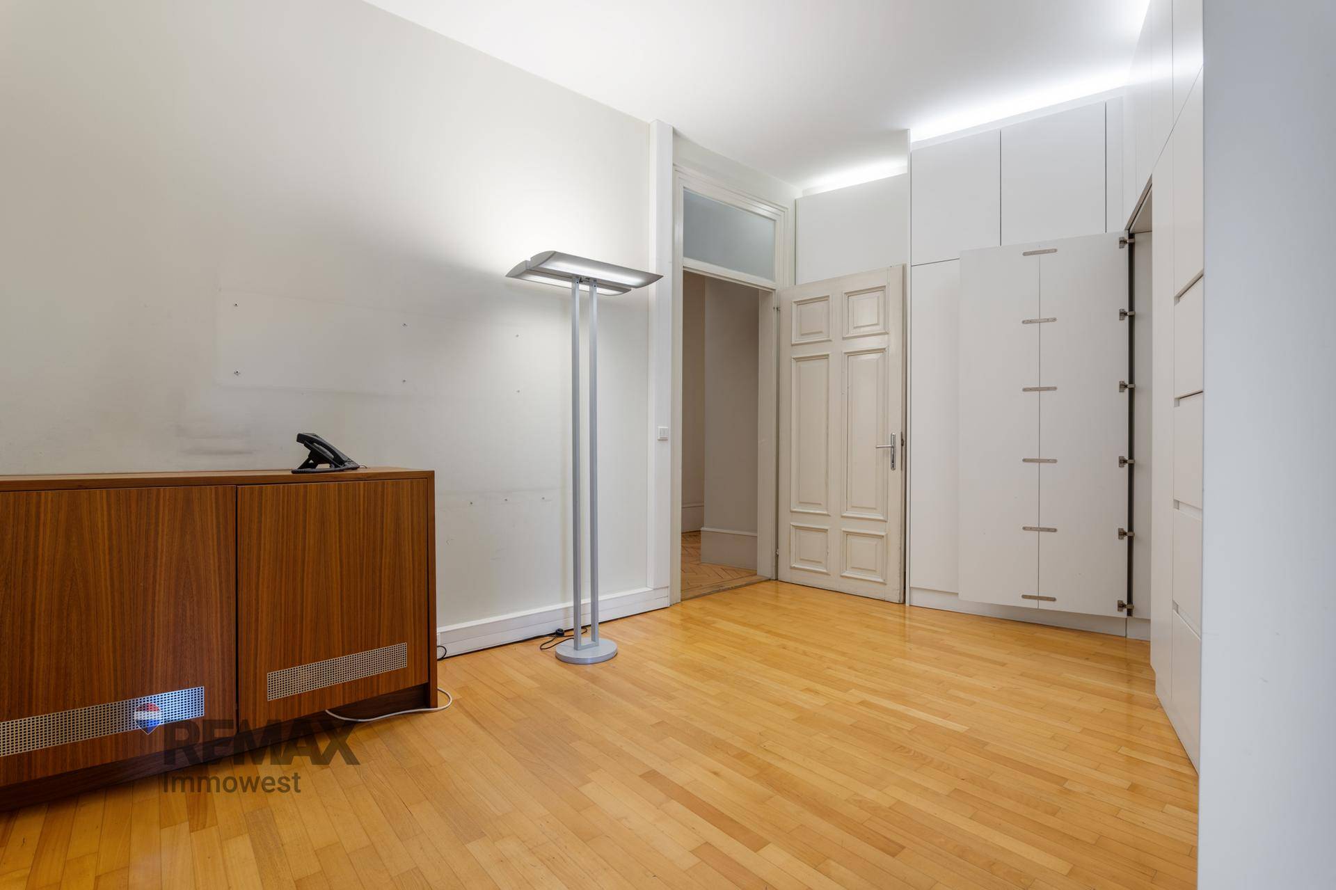 Modernes Büro mit Holzboden, Stehlampe und weißen Einbauschränken für viel Stauraum.