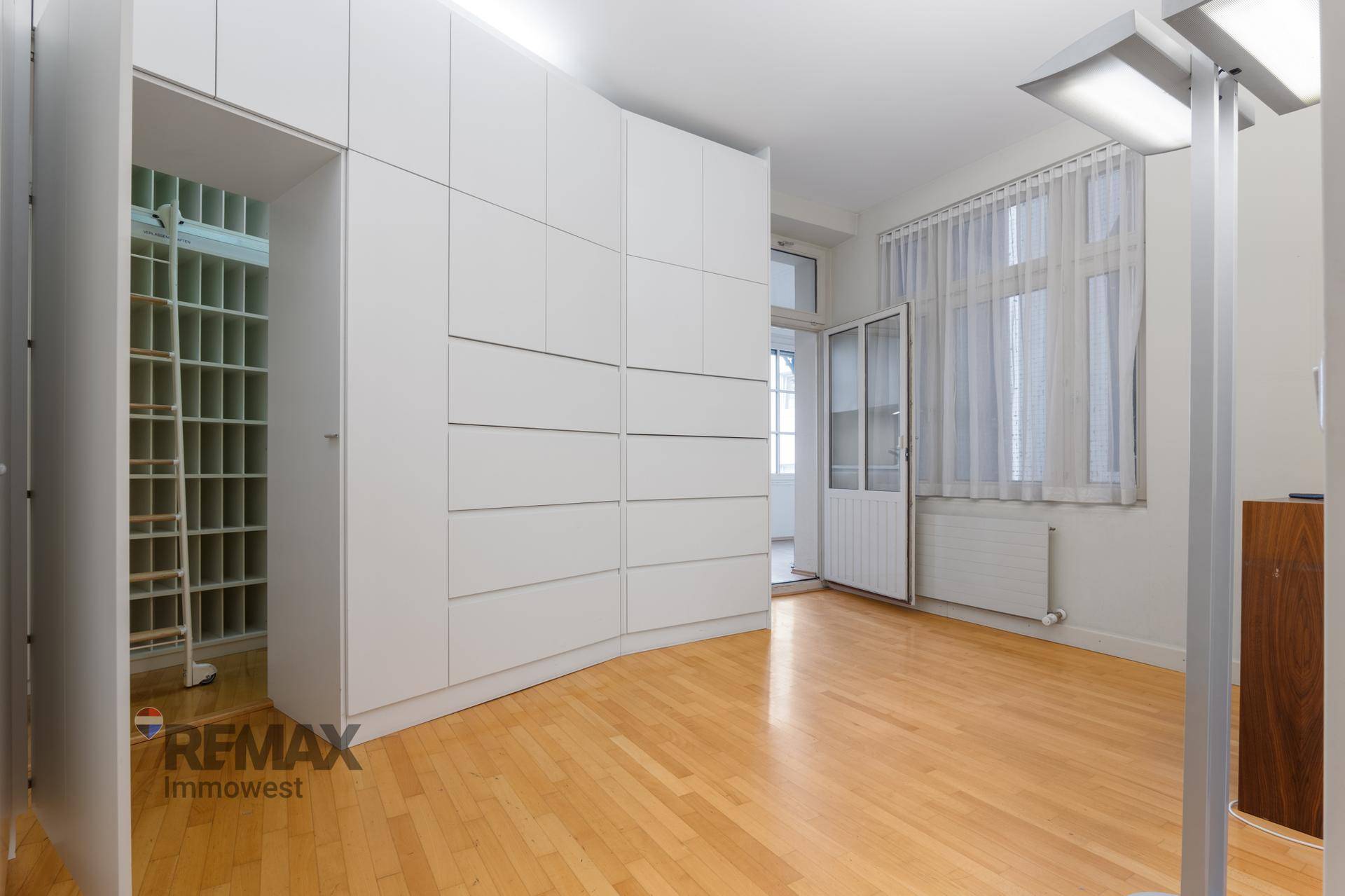 Geräumiges Büro mit Holzboden, weißen Einbauschränken und Zugang zu einem weiteren Raum.