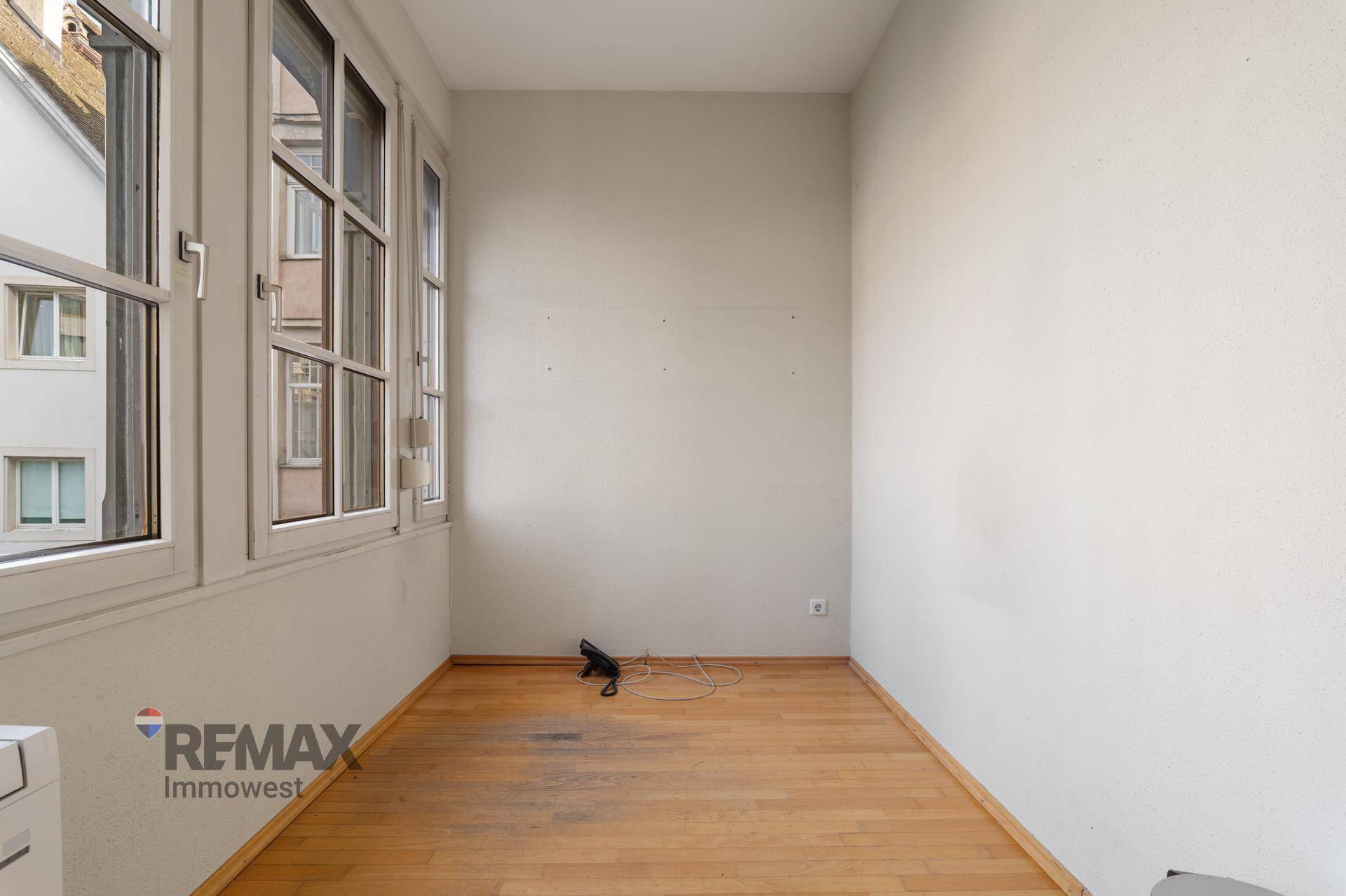 Kleiner Büroraum mit Holzboden und großen Fenstern, die viel natürliches Licht hereinlassen.