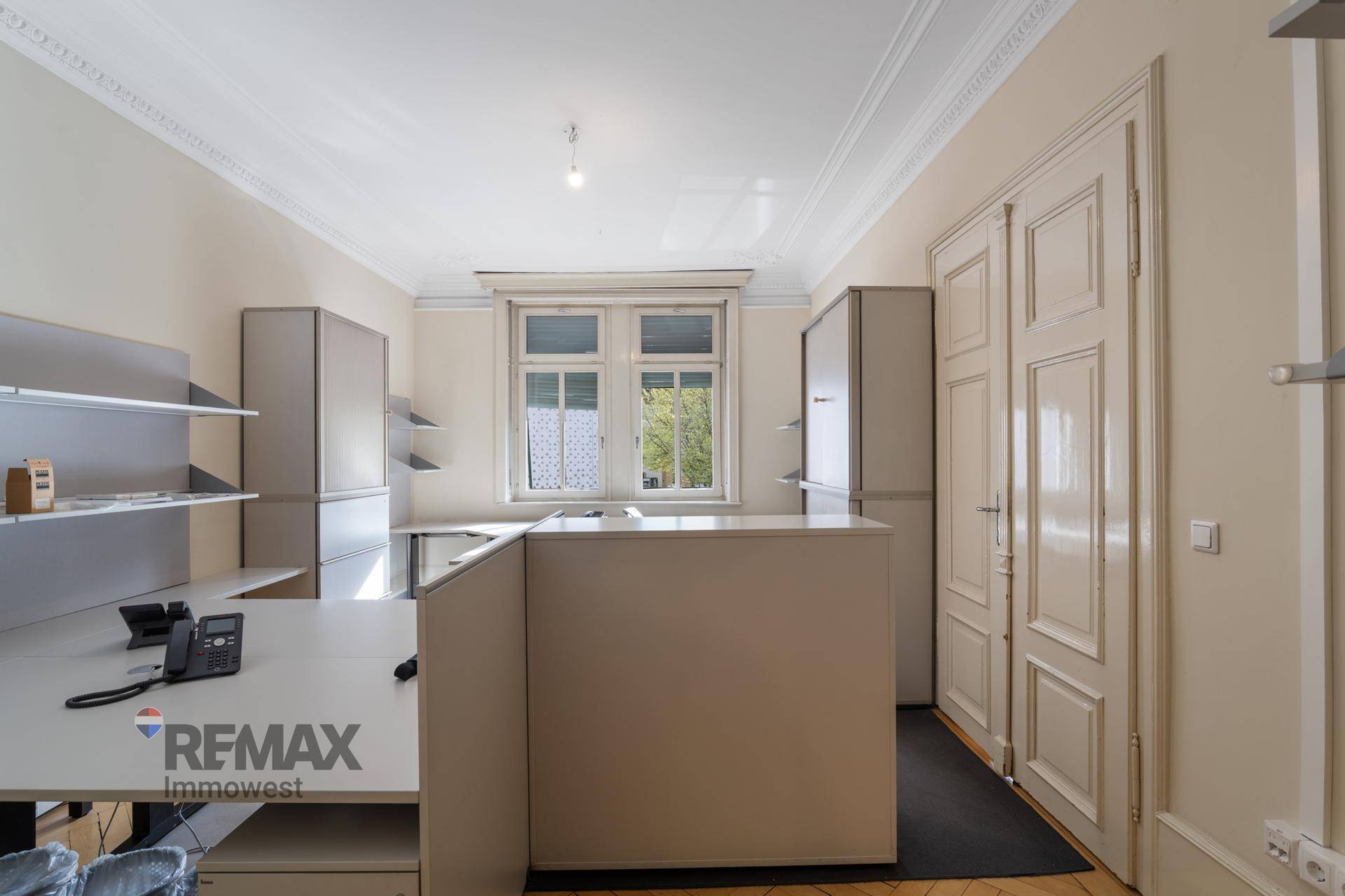 Büro mit hellem Holzboden, großen Fenstern und funktionalen Büromöbeln in neutralen Farben.