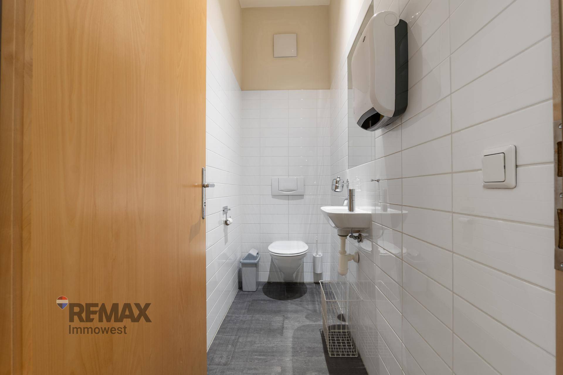 Modernes Gäste-WC mit weißen Fliesen, kleinem Waschbecken und dunklem Fliesenboden.