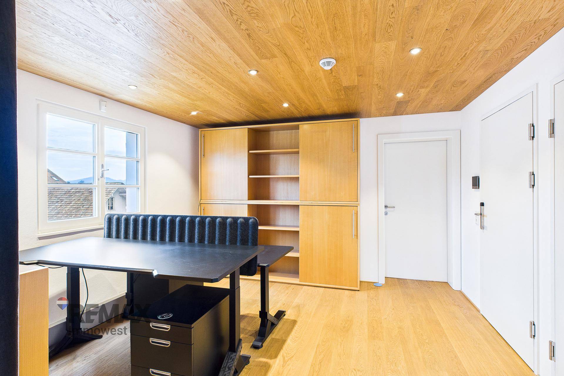 Büro mit Holzboden, Einbauschränken und einem Schreibtisch am Fenster mit Bergblick.