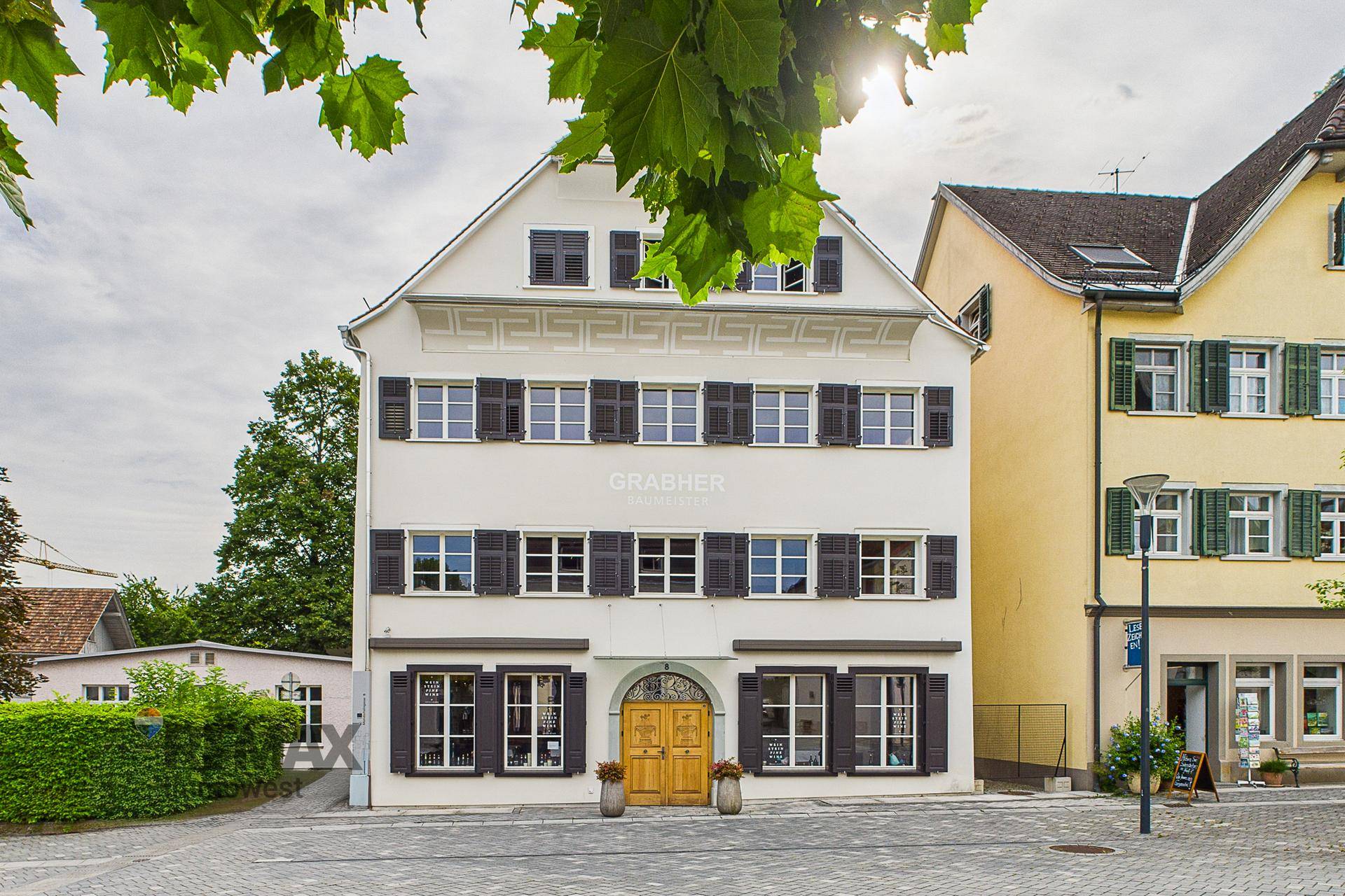 Historisches Gebäude mit weißer Fassade, vielen Fenstern und dunklen Fensterläden.