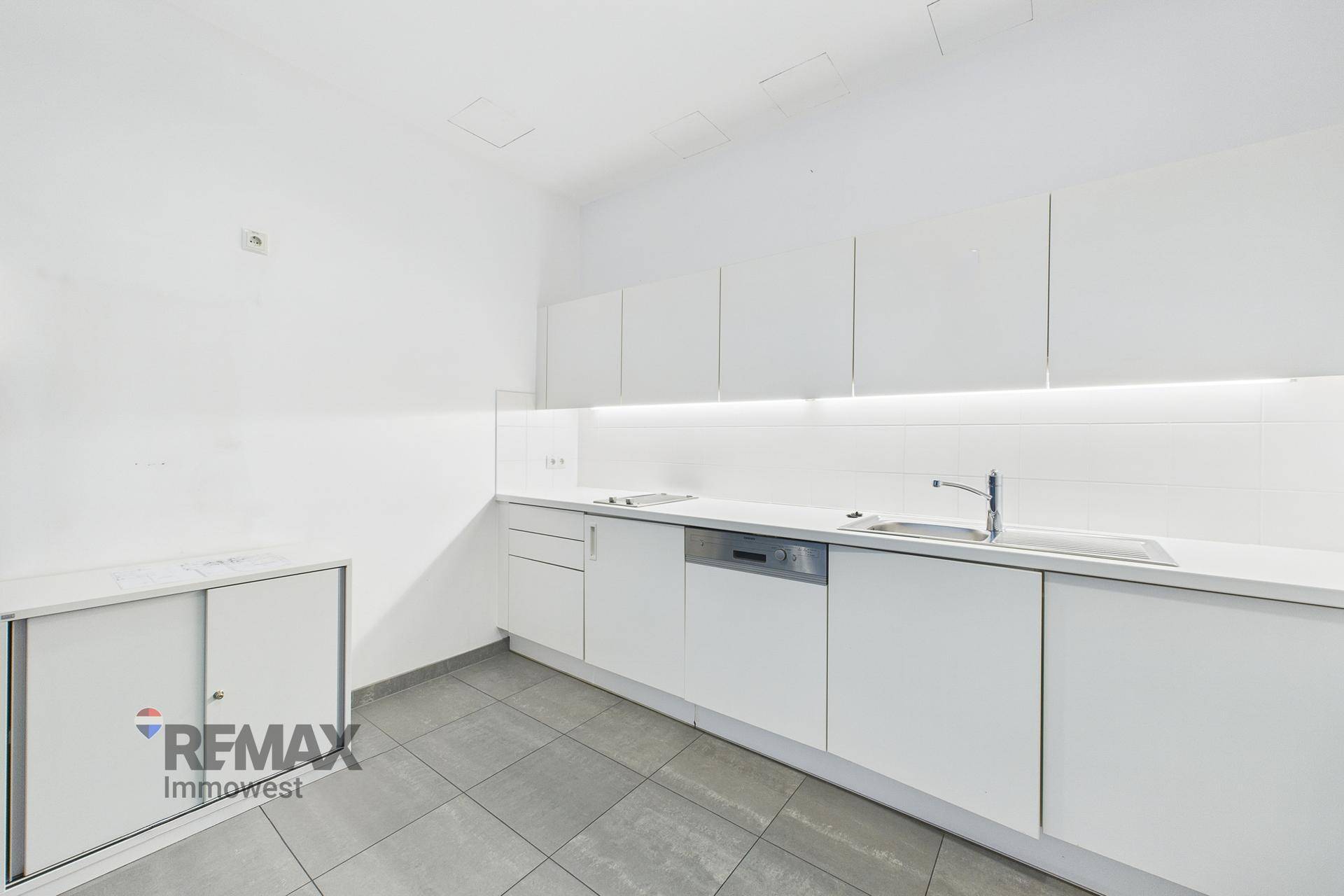 Moderne Einbauküche mit weißen Schränken, Spülmaschine und Fliesenboden.