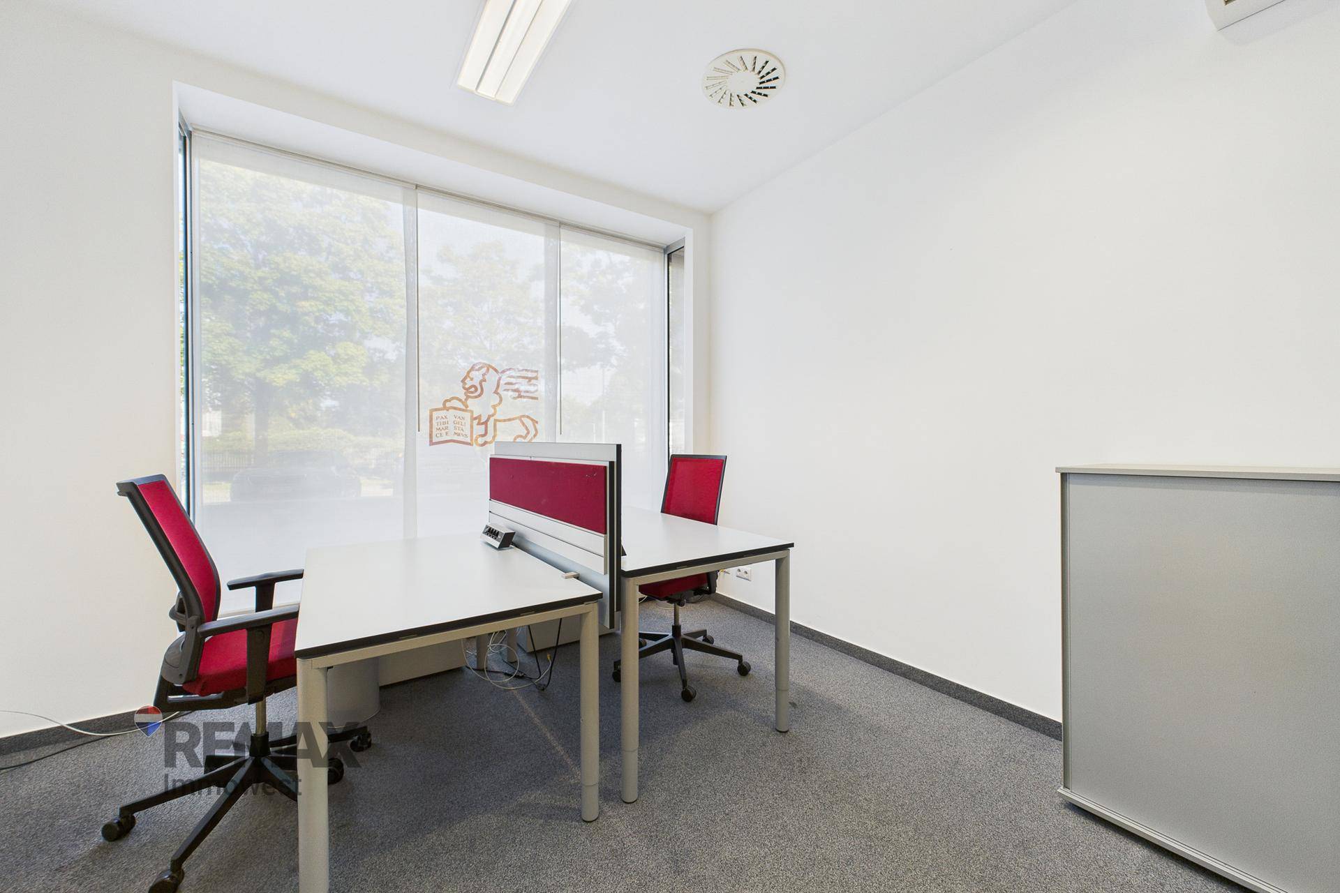 Helles Büro mit zwei Arbeitsplätzen, Teppichboden und großen Fenstern.