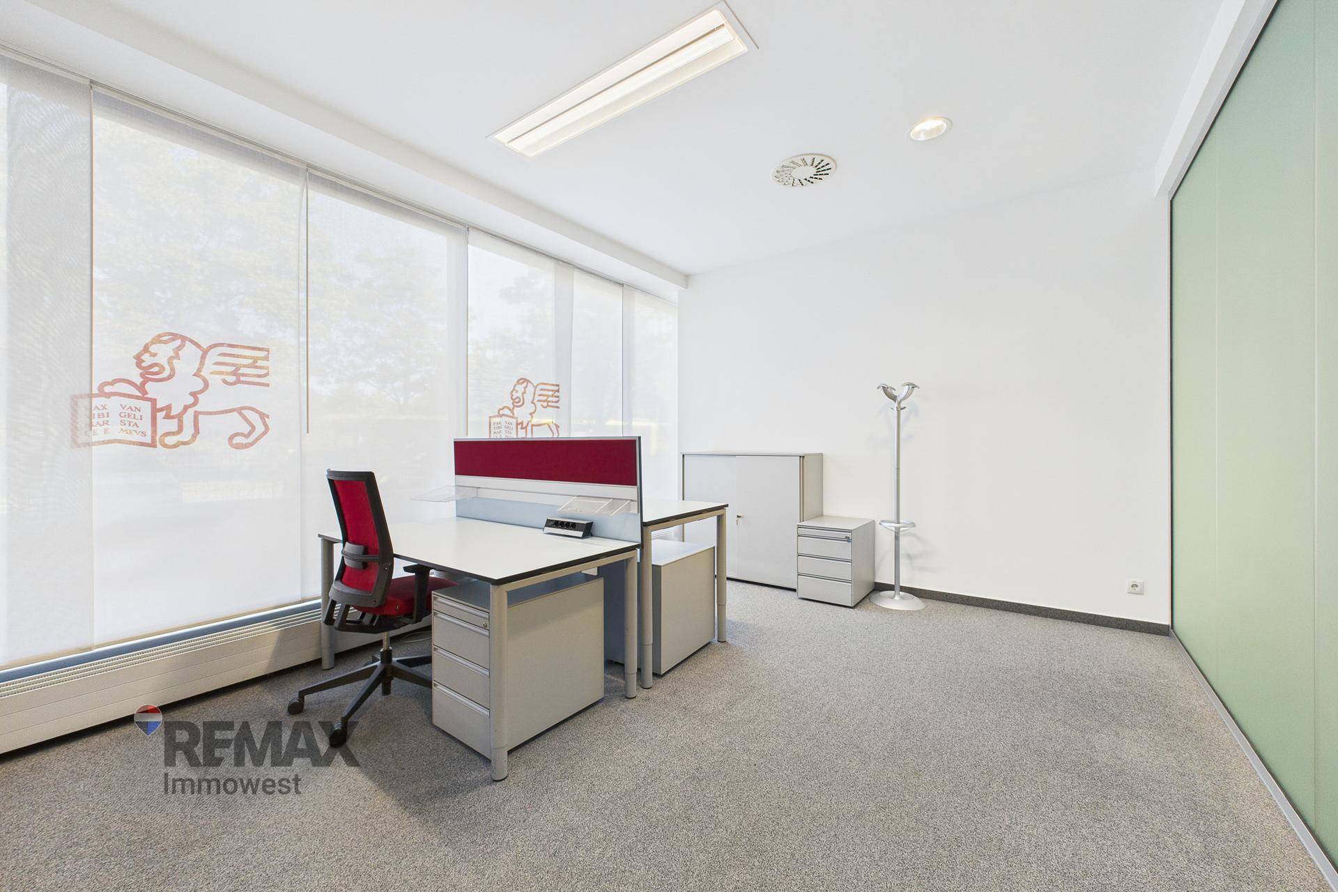 Einzelner Arbeitsplatz in einem hellen Büro mit Teppichboden und Blick nach draußen.